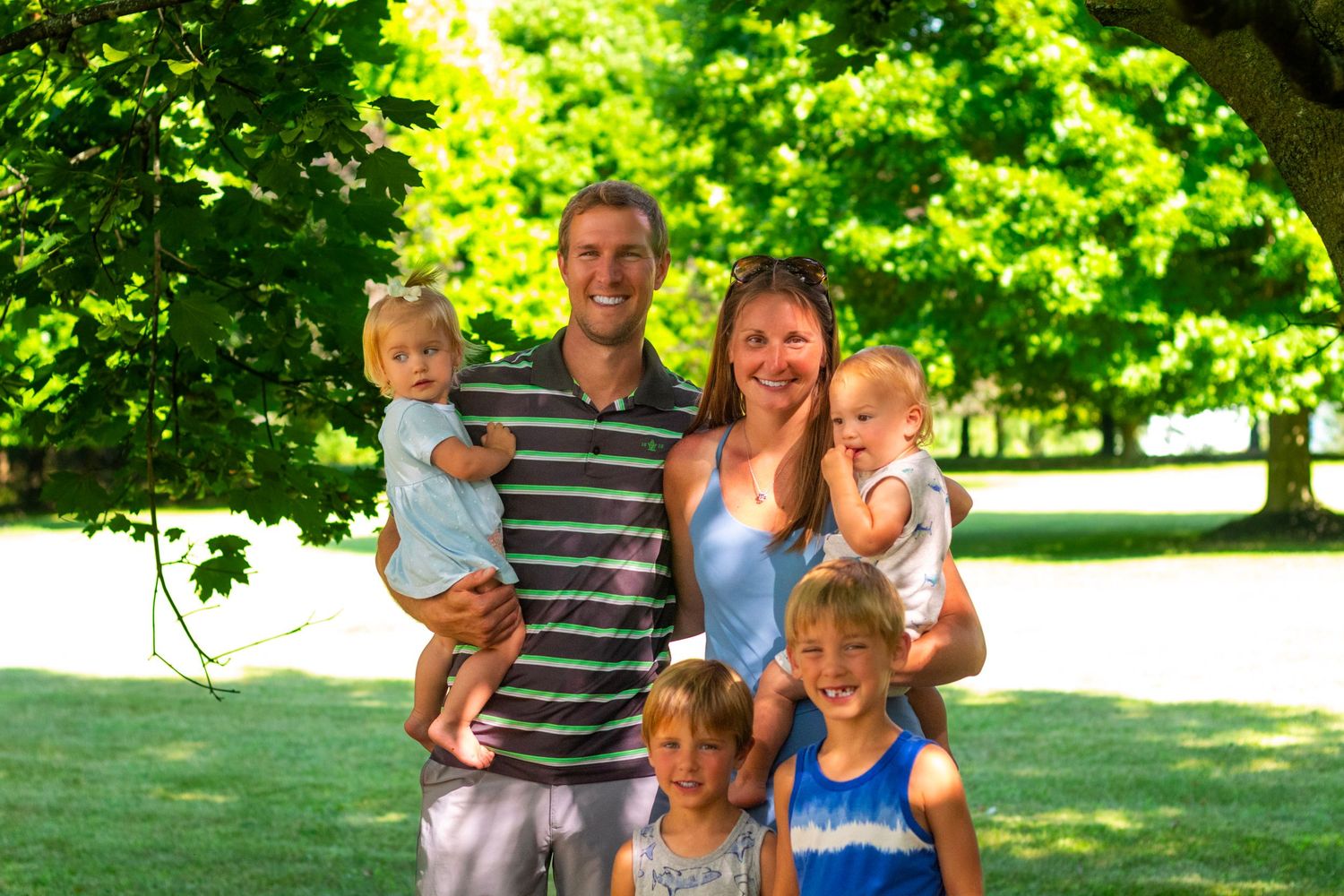 Family of six posing together under a green leafy tree on a sunny day.