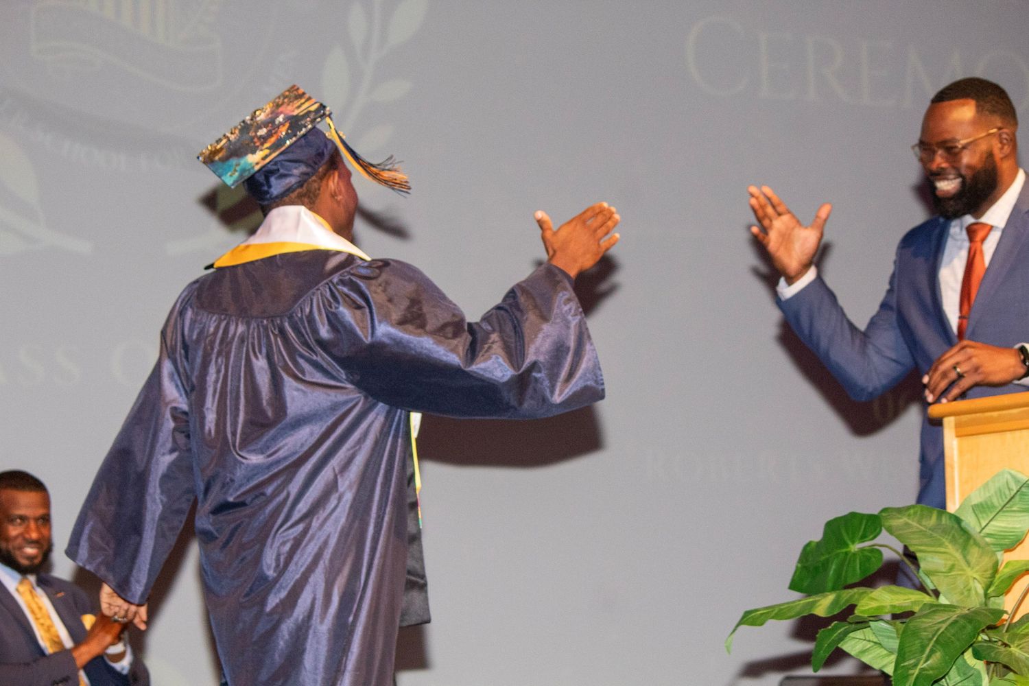 People in graduation robes and formal attire celebrating with enthusiastic gestures on stage.