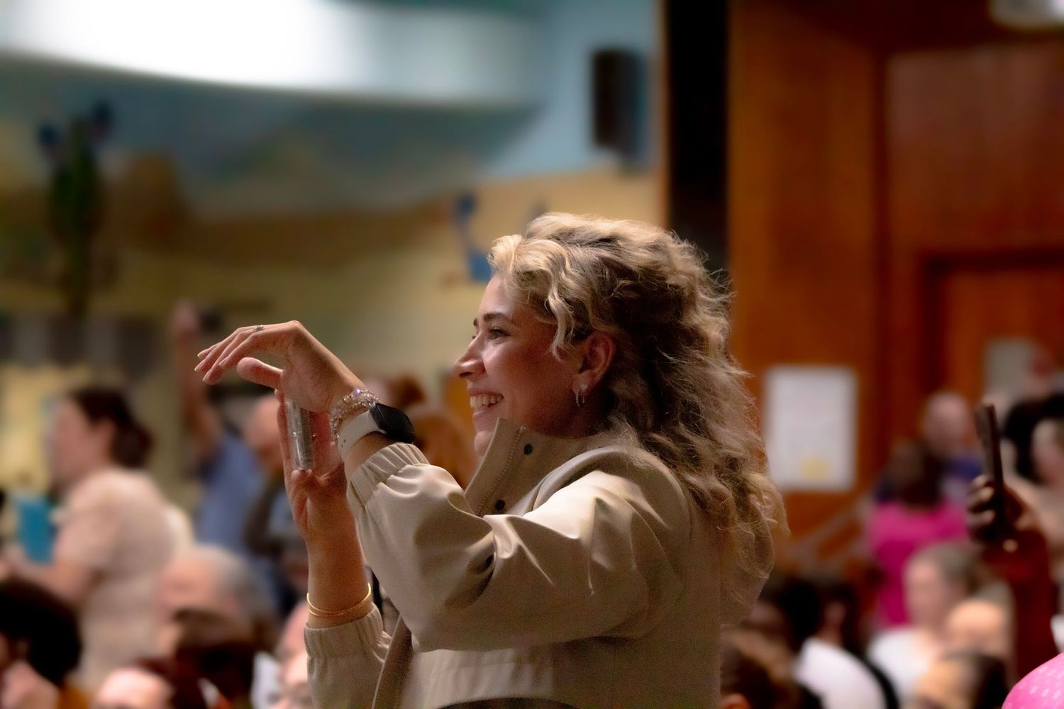 Person gesturing enthusiastically while speaking in an auditorium setting.
