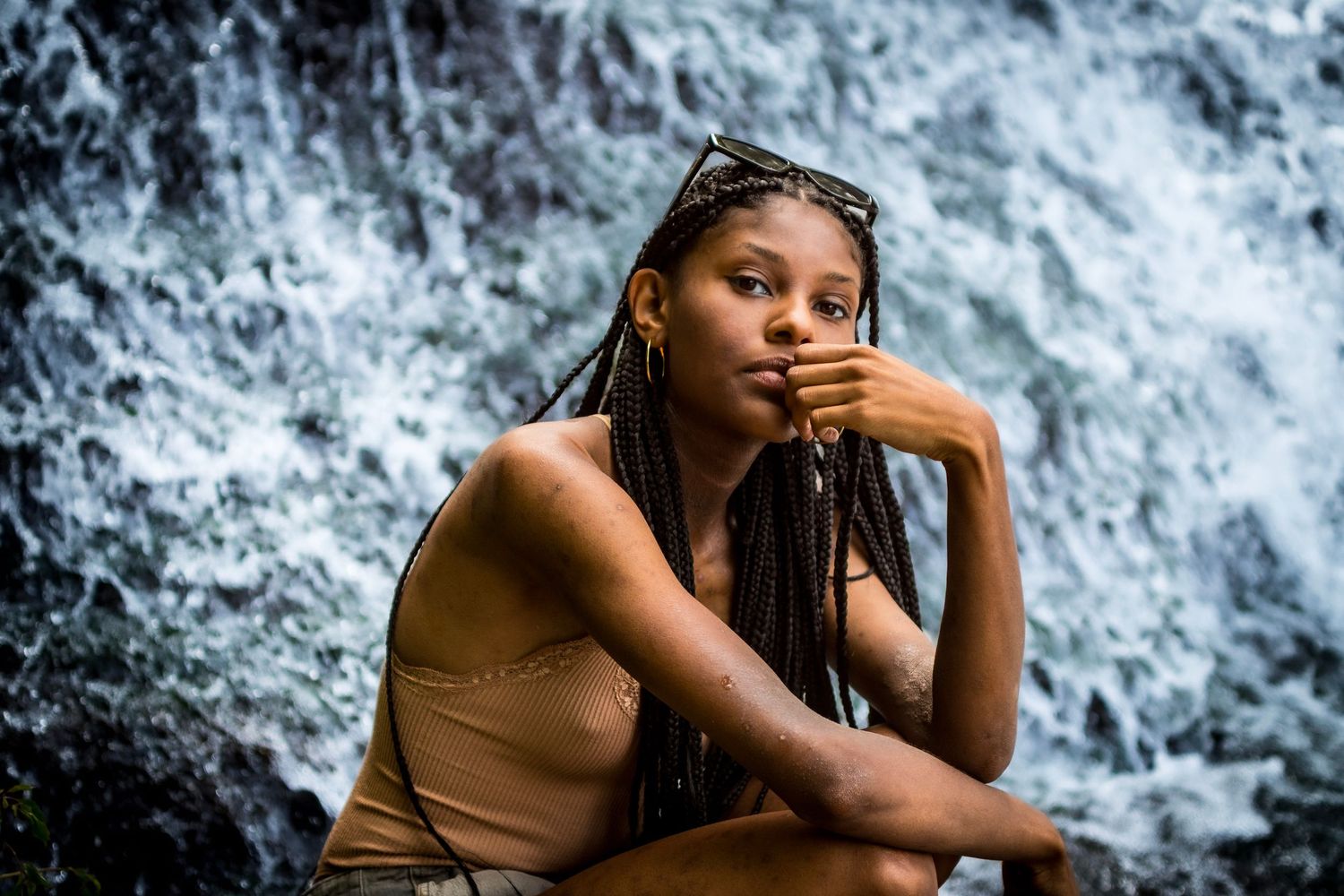 Portrait of person with braids posing thoughtfully by waterfall.