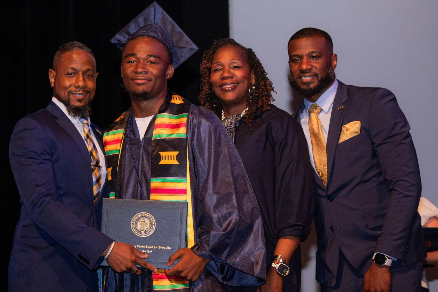 Graduate in colorful stole poses with supporters at graduation ceremony.