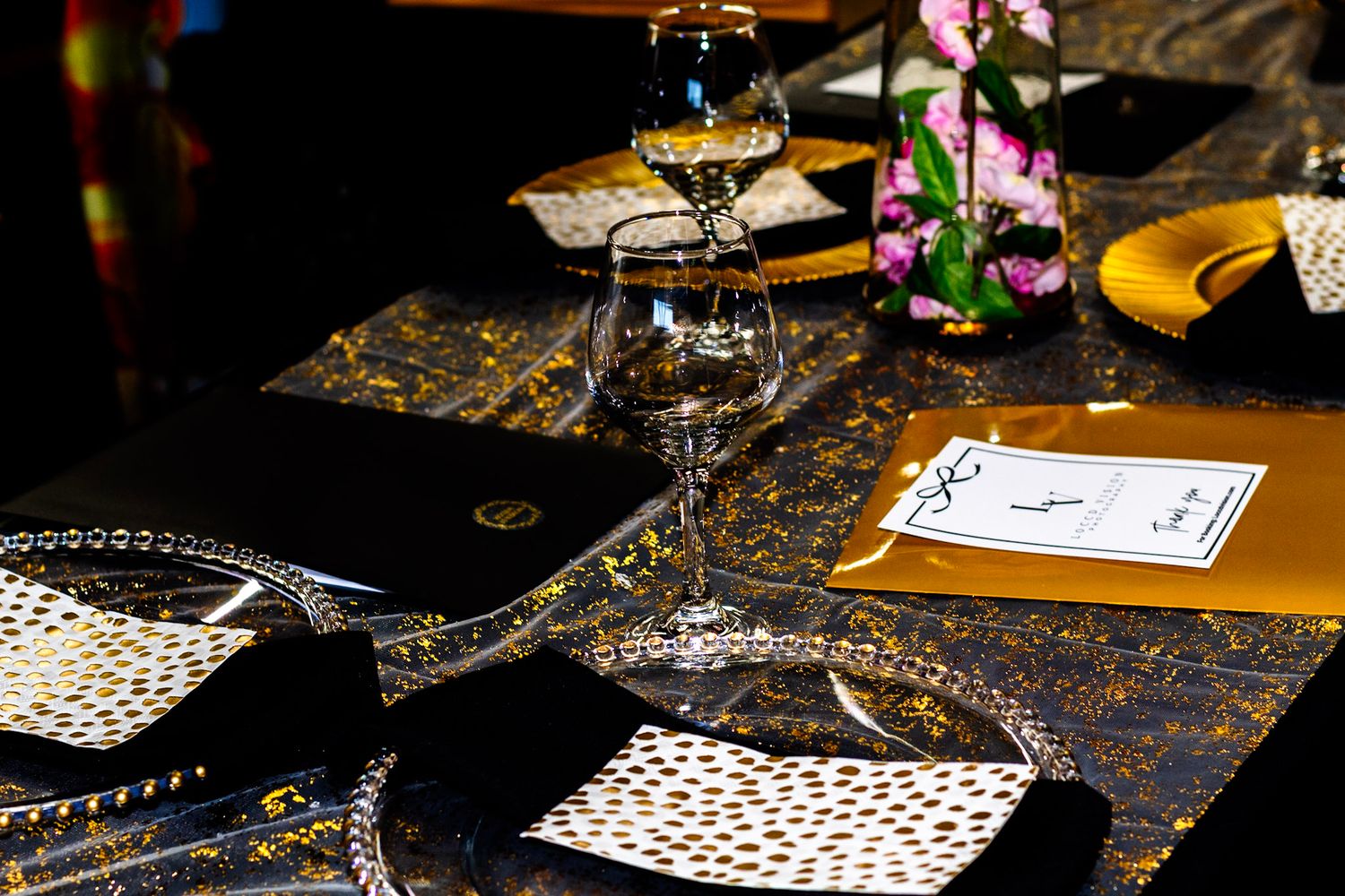 Elegant table setting with tiered serving dishes, wine glasses and patterned placemats.