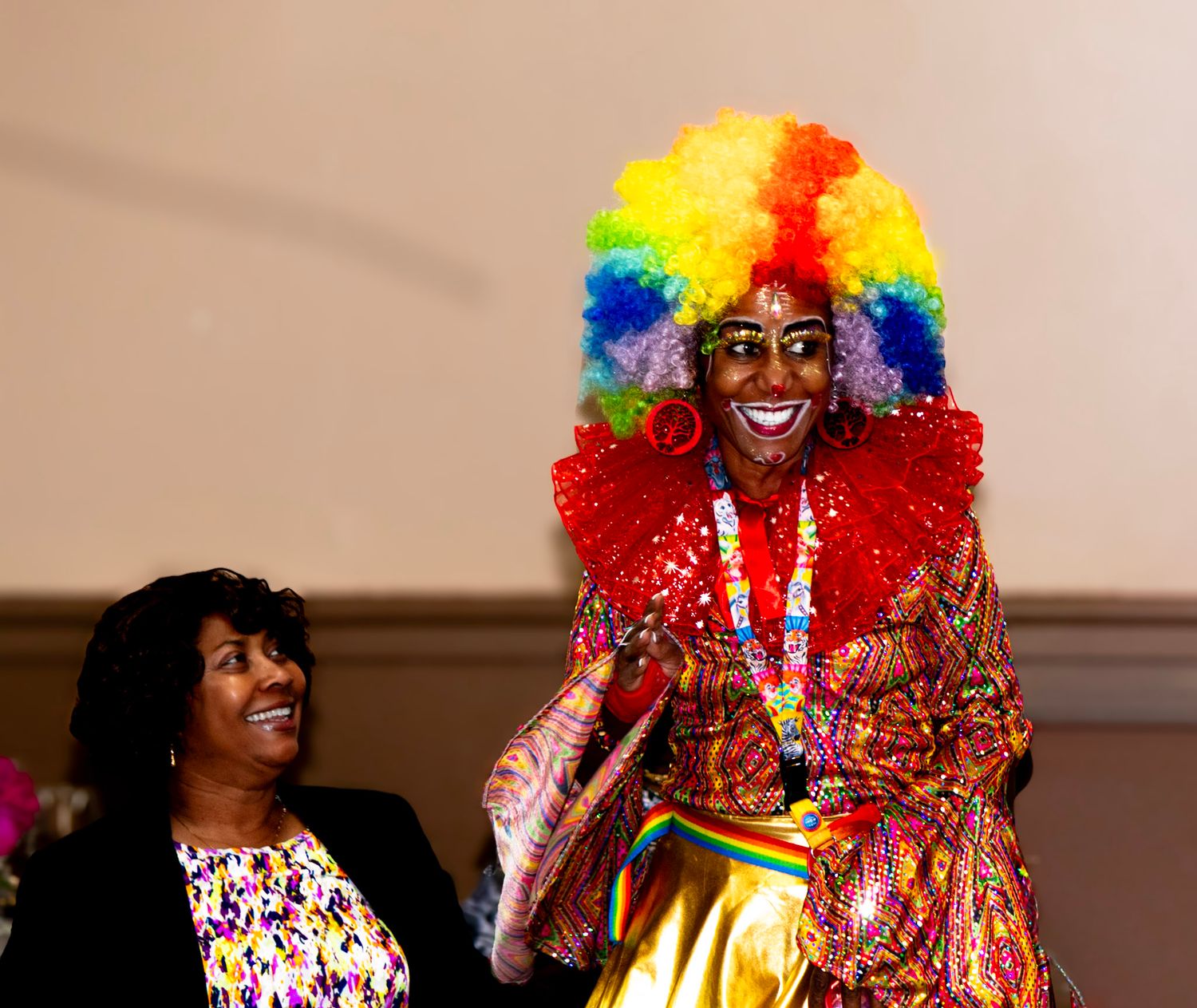 Performer wearing colorful rainbow wig and sparkly red costume entertaining at an event.