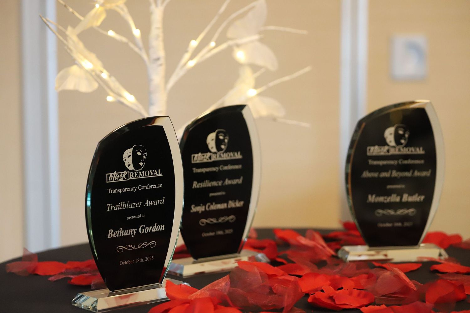 Row of black glass awards displayed on red fabric.