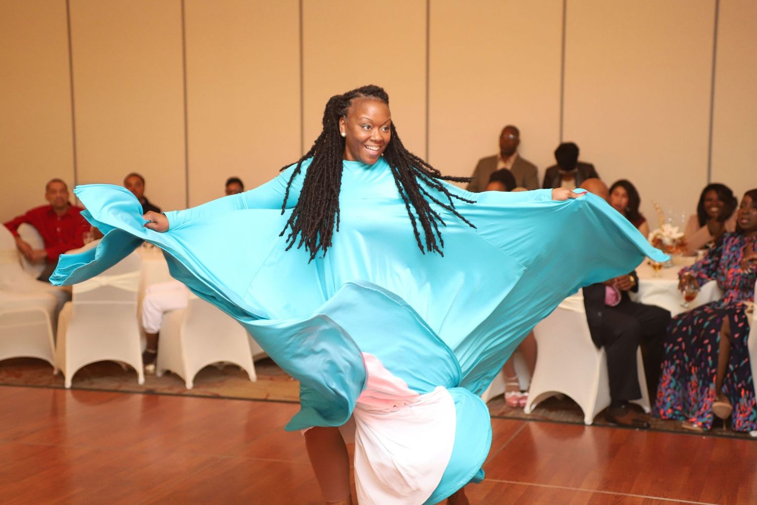 A dancer performs gracefully in a flowing turquoise dress on a wooden dance floor.