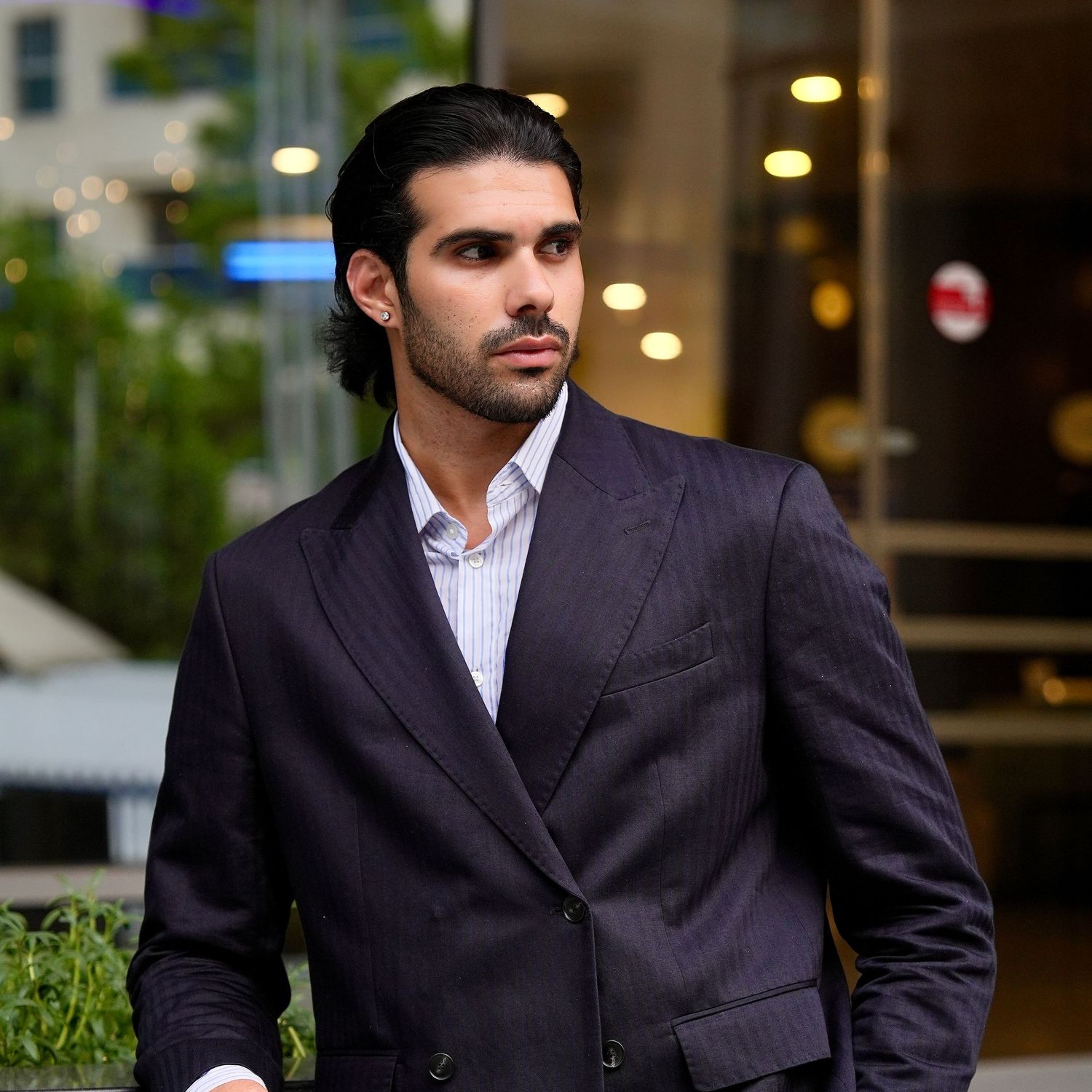 Professional wearing a dark suit and white shirt poses confidently in an outdoor business setting.