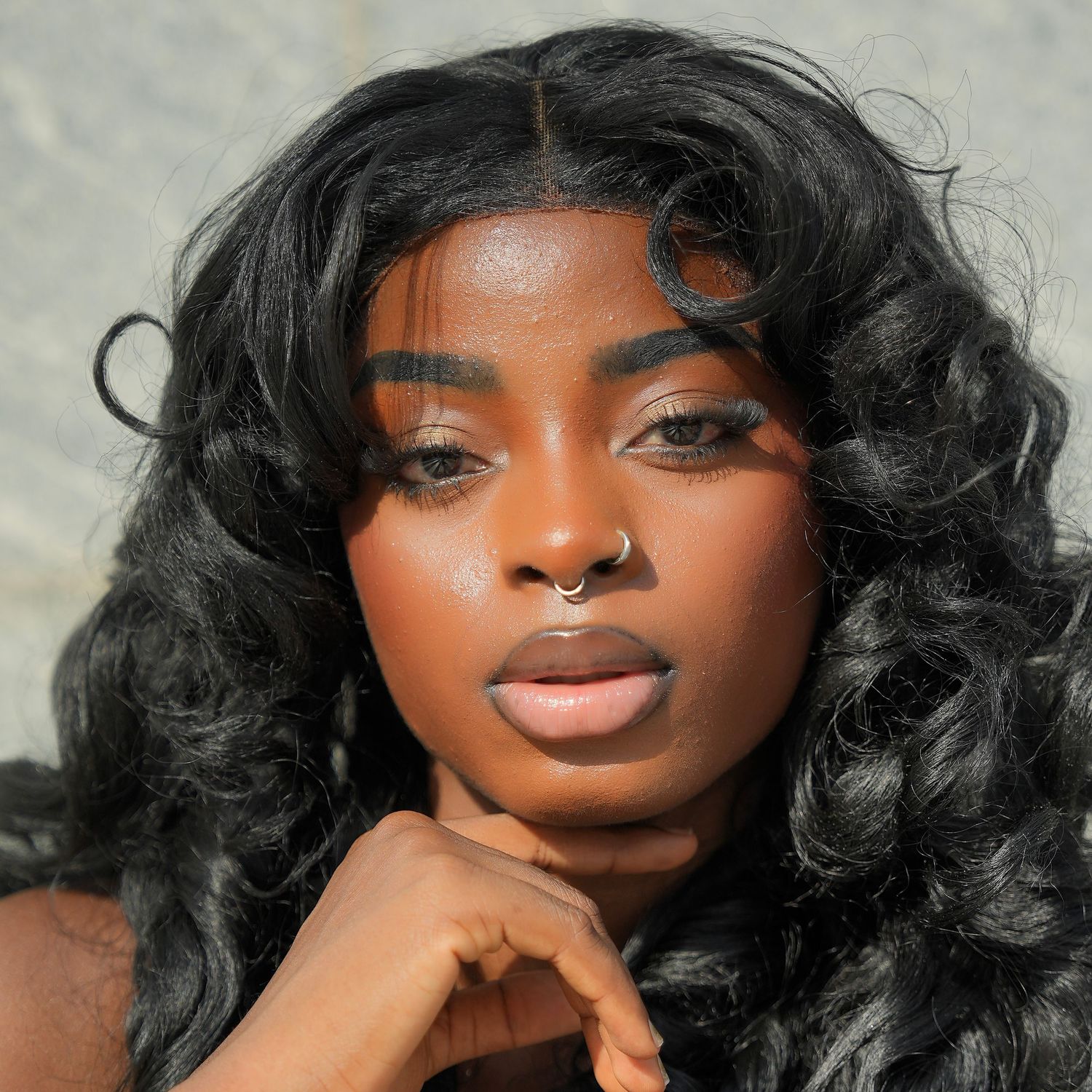 Close up beauty portrait with glamorous curly black hair, septum piercing and soft makeup in natural lighting.