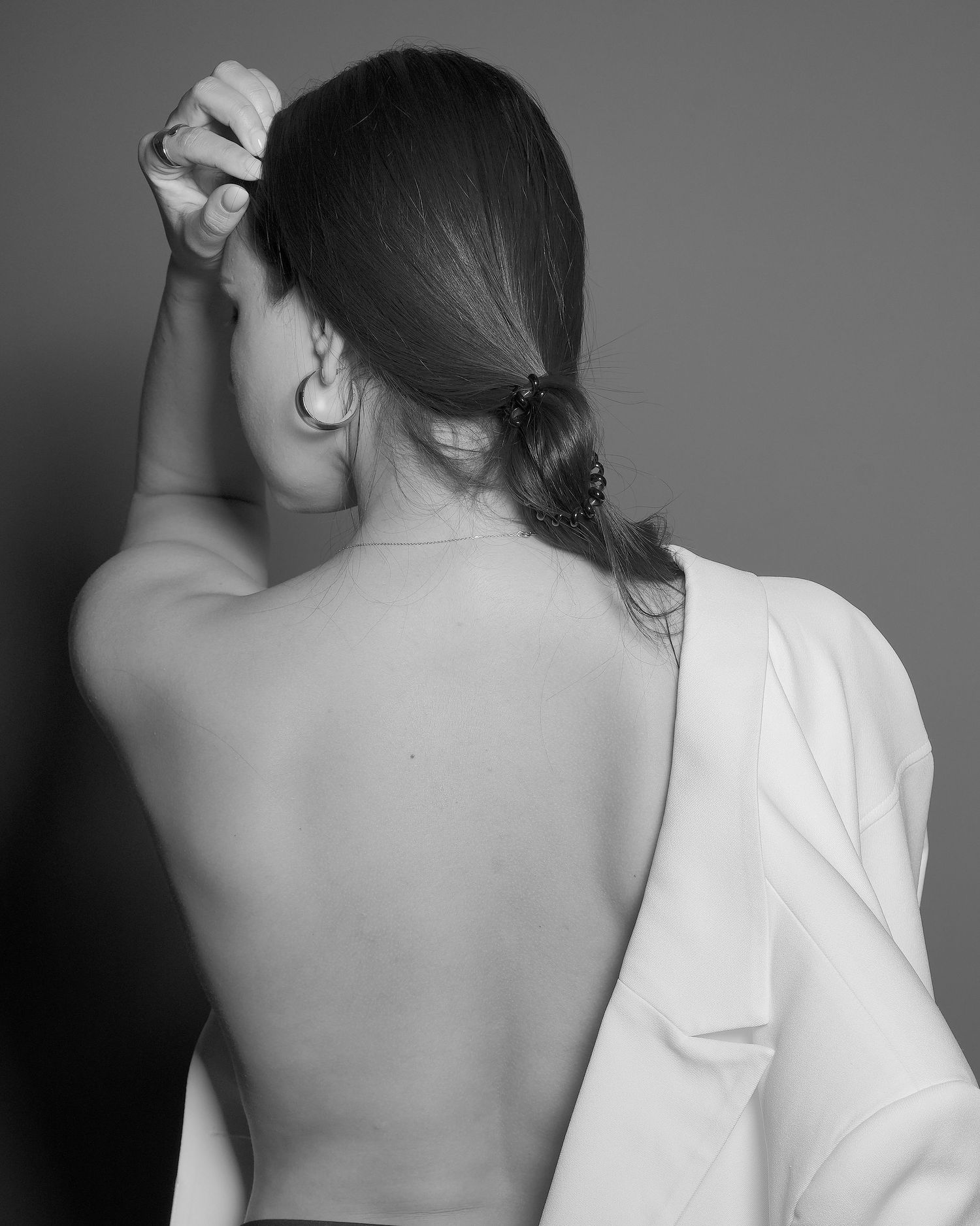Artistic black and white portrait showing a person's bare back with a partially removed white shirt and pulled back dark hair.