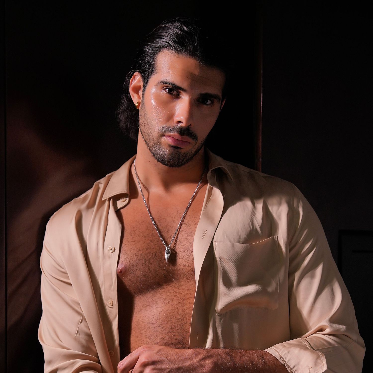Person in beige blazer poses in dramatic lighting against dark background for fashion photography series.