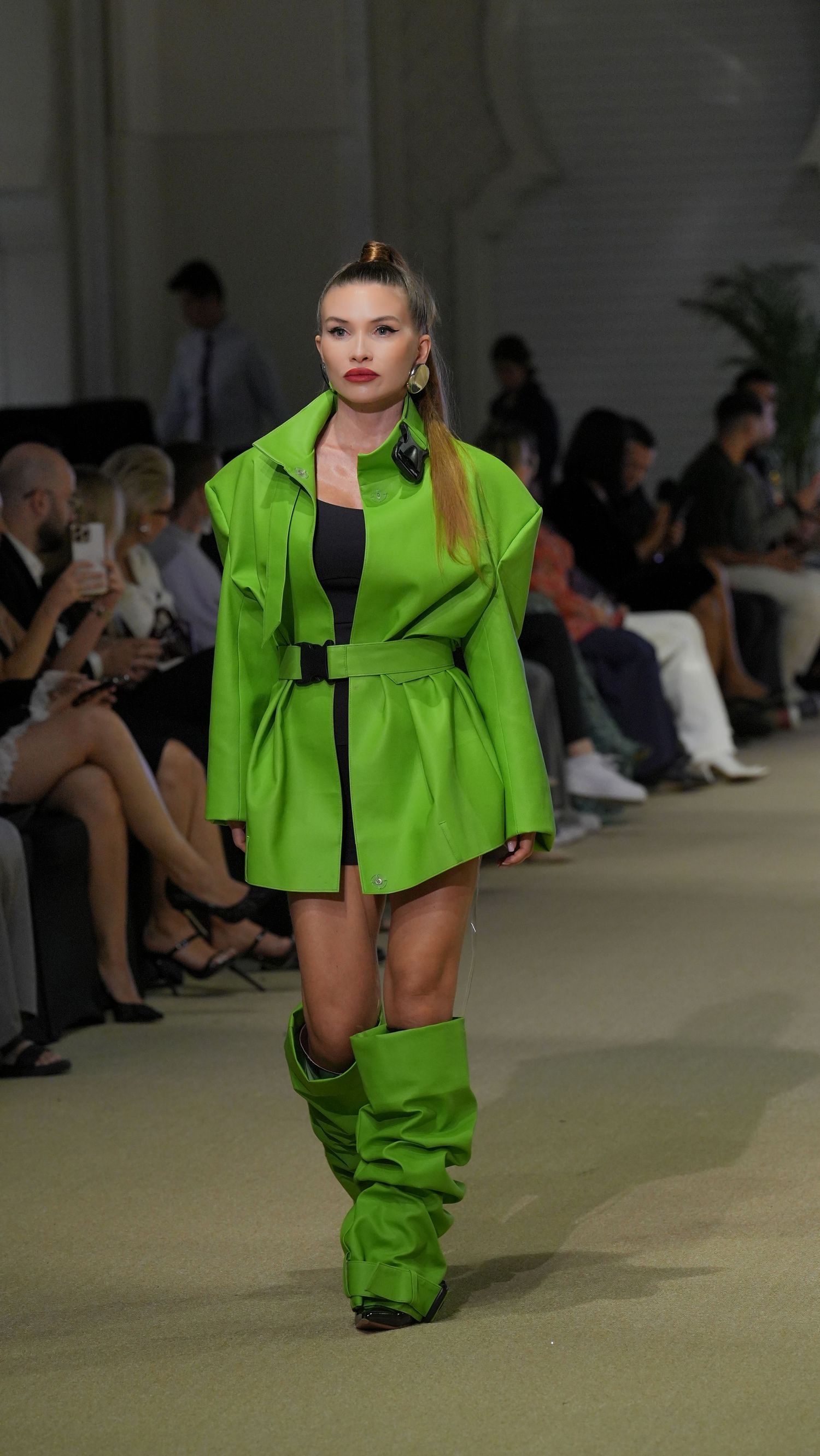 Model walks runway in vibrant neon green cropped jacket and baggy pants during fashion show presentation.