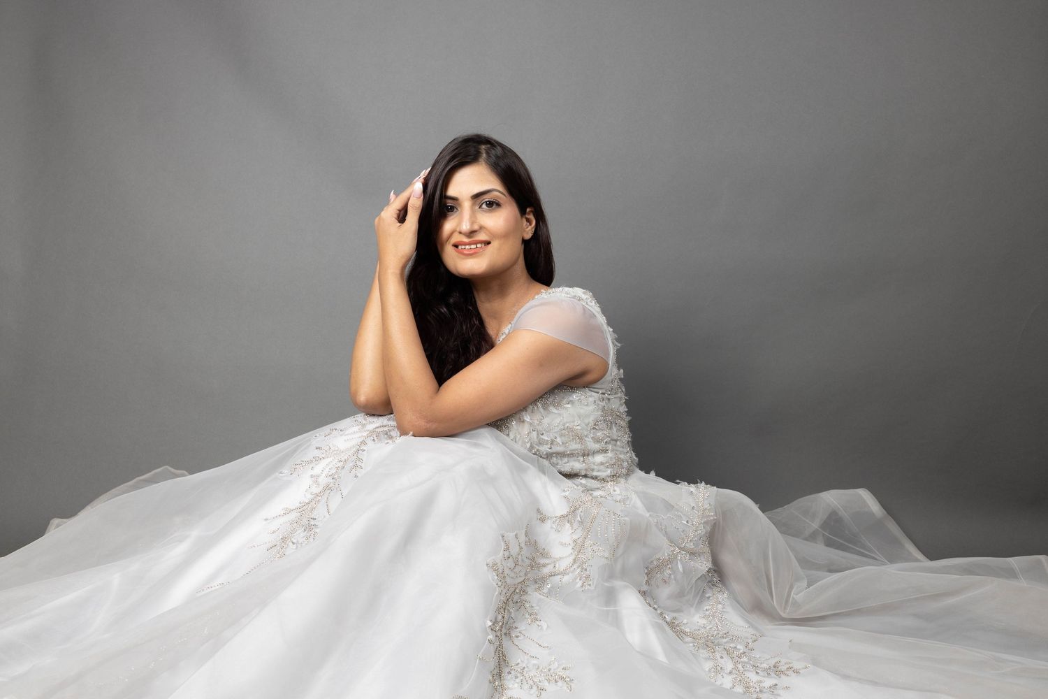 Elegant bridal portrait with flowing white wedding dress against grey backdrop.