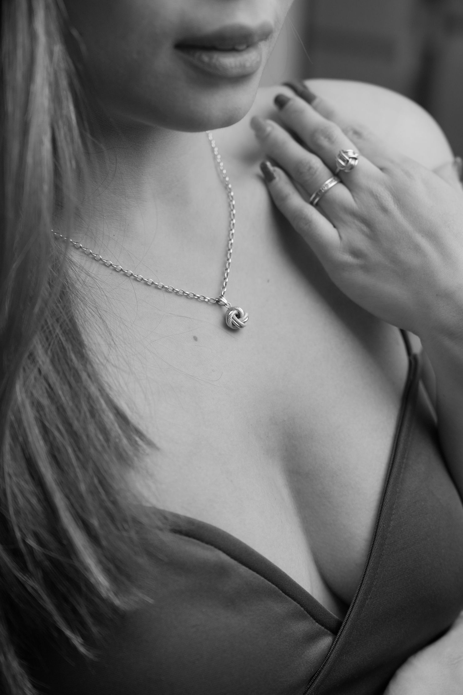 Black and white close-up of delicate necklace and ring jewelry against feminine neckline and long hair.