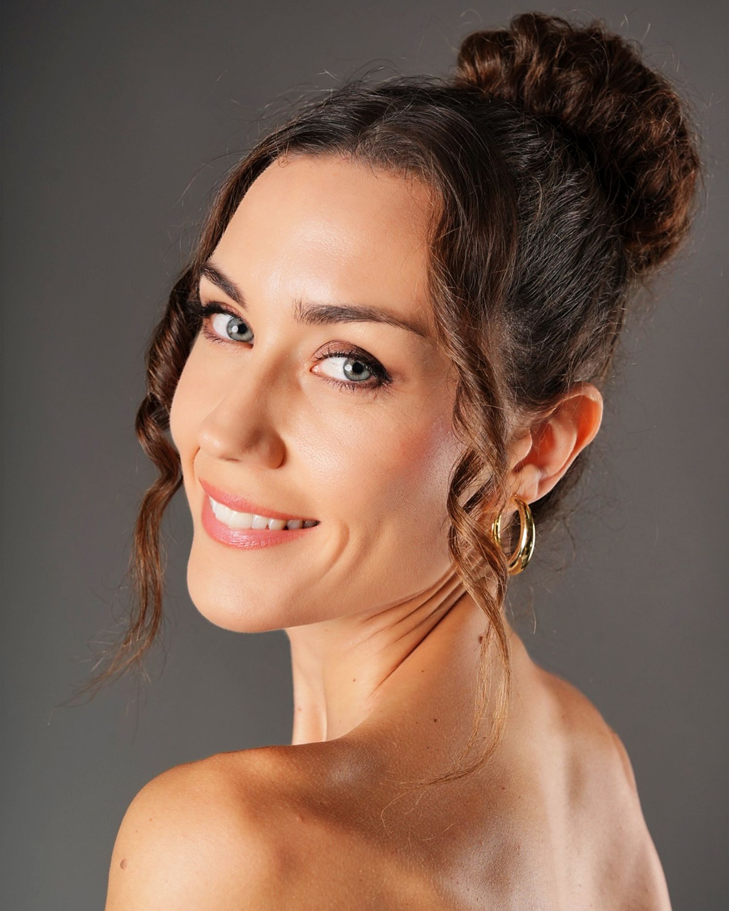 Professional headshot of a young woman with dark hair in a bun, wearing gold hoop earrings, smiling confidently.