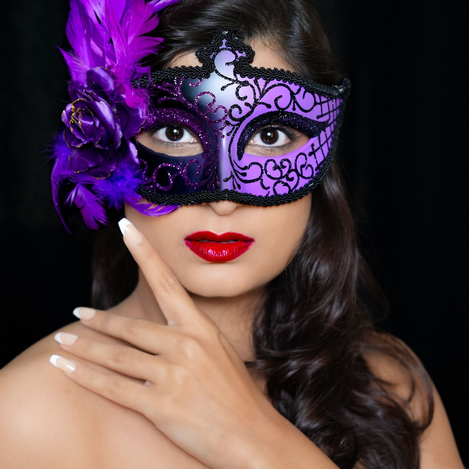 Woman wearing an ornate purple masquerade mask with flower detail and bold red lipstick in dramatic lighting.