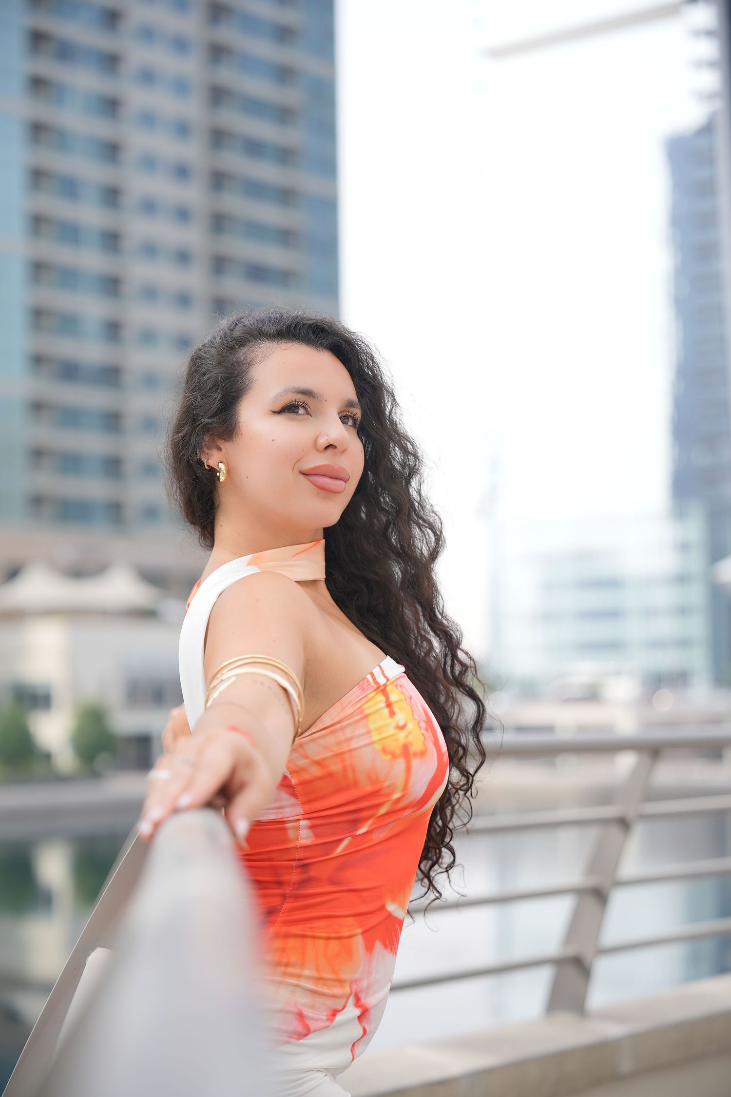 Fashion portrait in orange top against modern urban cityscape with glass buildings.