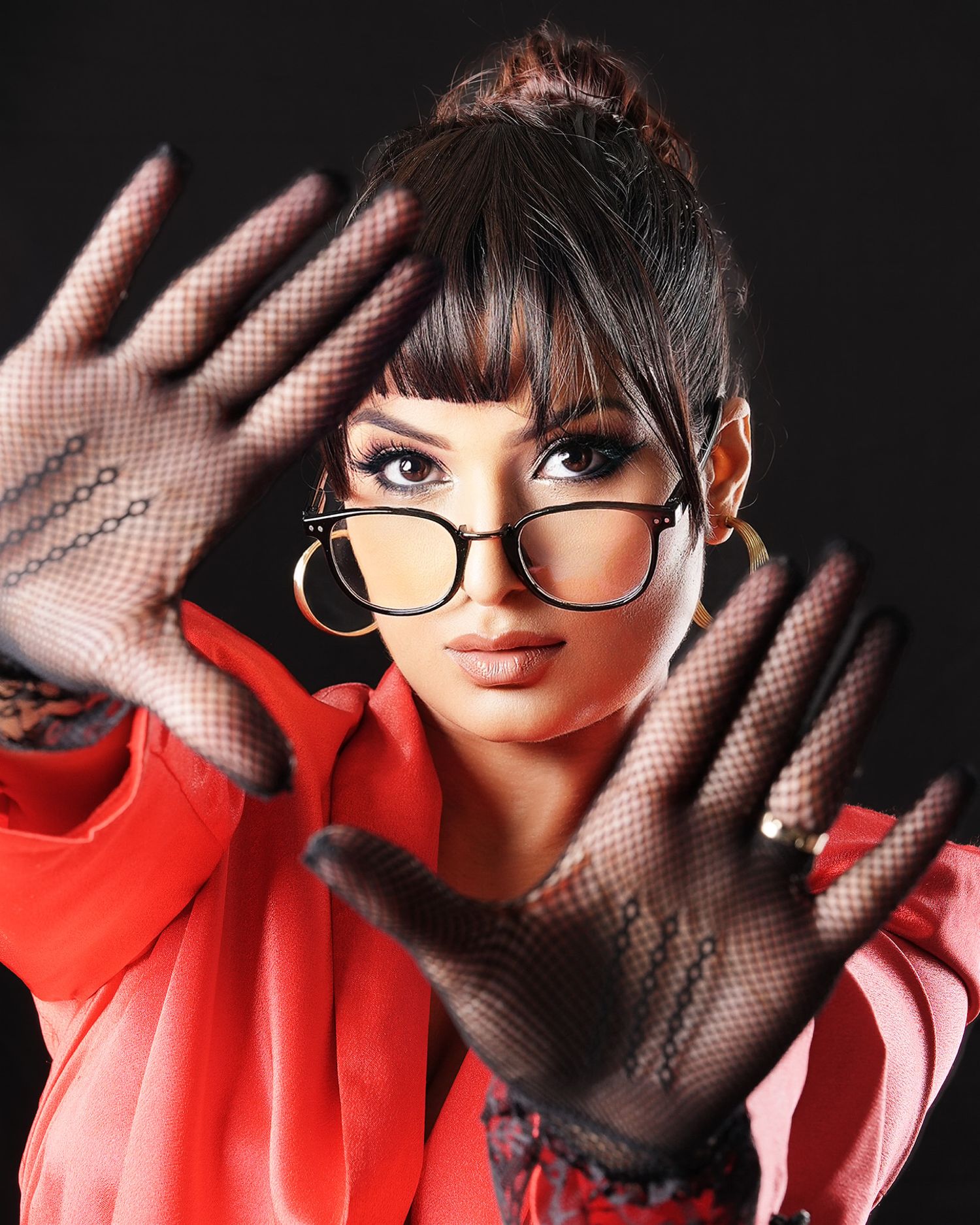 Woman in red outfit, fishnet gloves, and retro glasses poses with hands raised toward camera.
