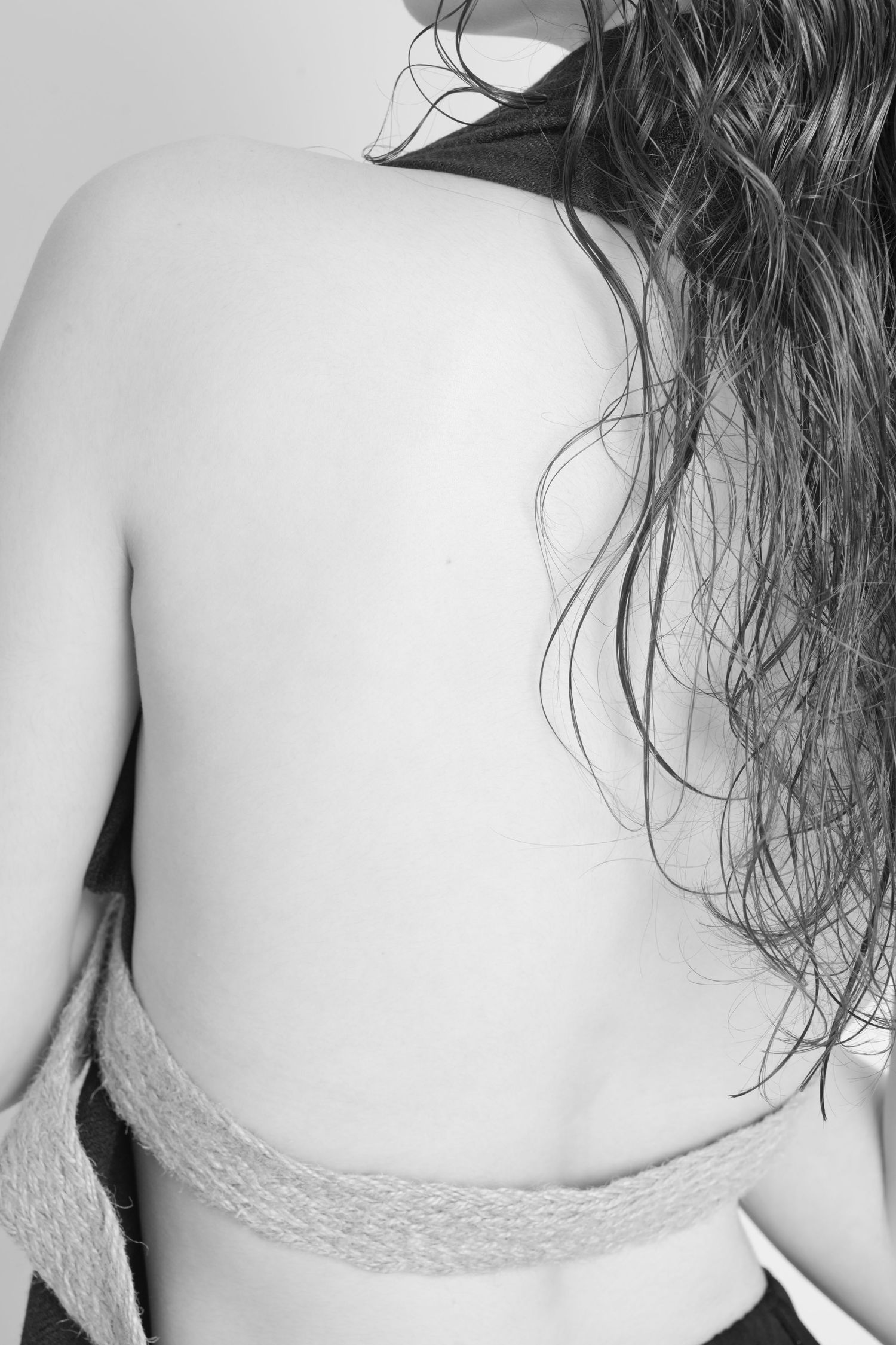 Black and white artistic photograph showing a bare back with long wavy dark hair and lace trim detail.