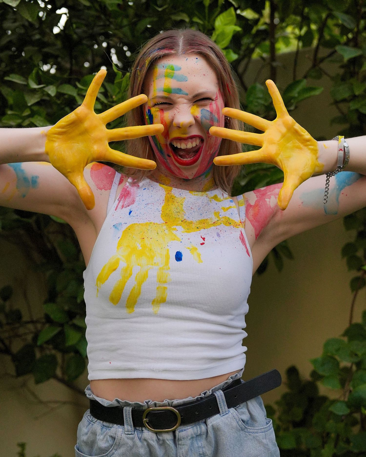 A series of photos showing a person in a white crop top with colorful paint-stained hands expressing joyful energy.