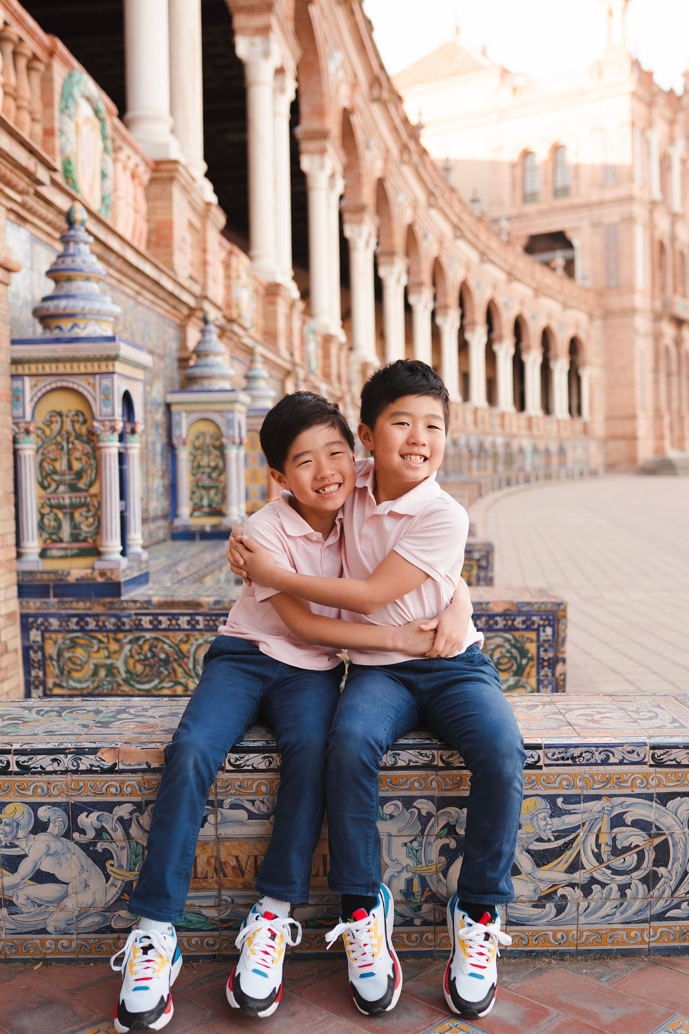 Two Asian brothers hugging and smiling on a decorative tiled bench at Plaza de Espana Seville.