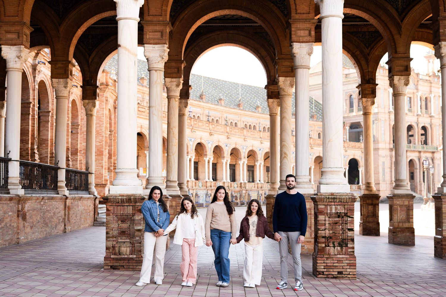 Family of five posing under arched colonnade at Plaza de España, Seville, Spain.