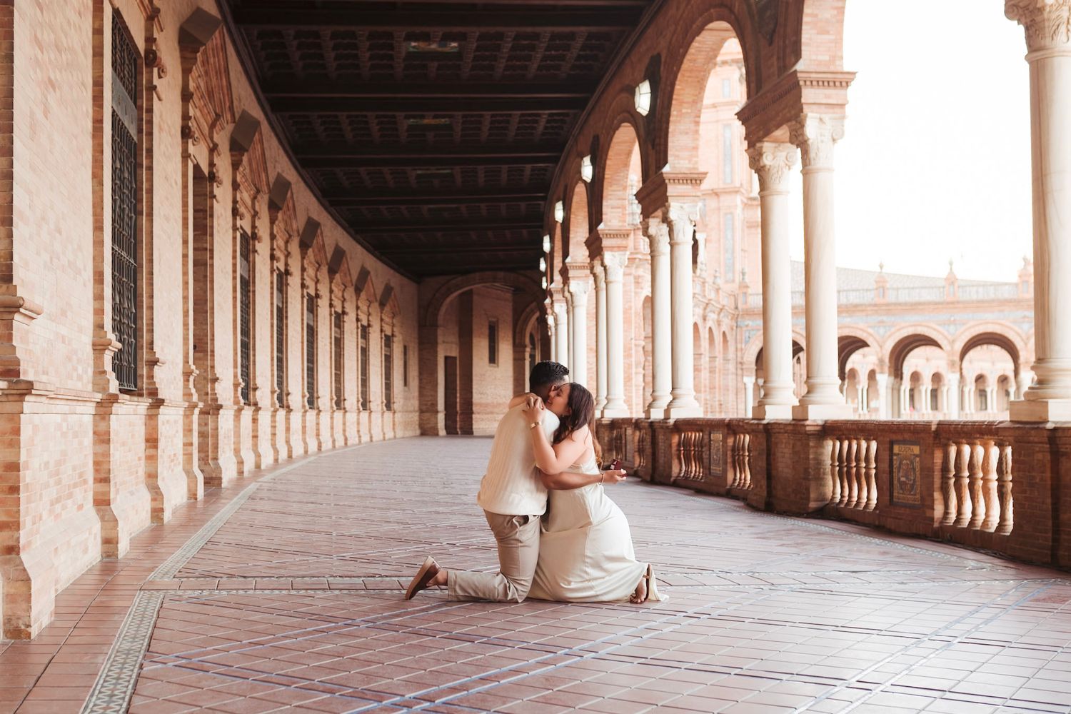 Couple embraces after proposal in stunning Plaza de España colonnade arcade in Seville Spain.