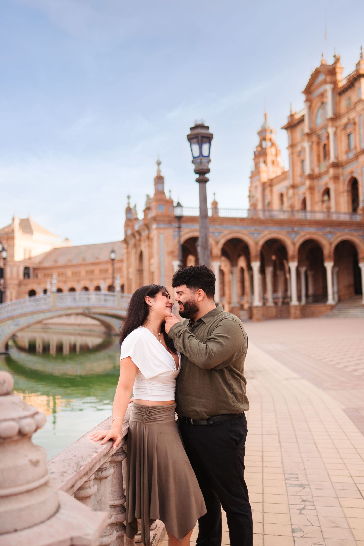 Romantic couple sharing a tender moment at Plaza de España in Seville, Spain, with ornate architecture and canal in background.