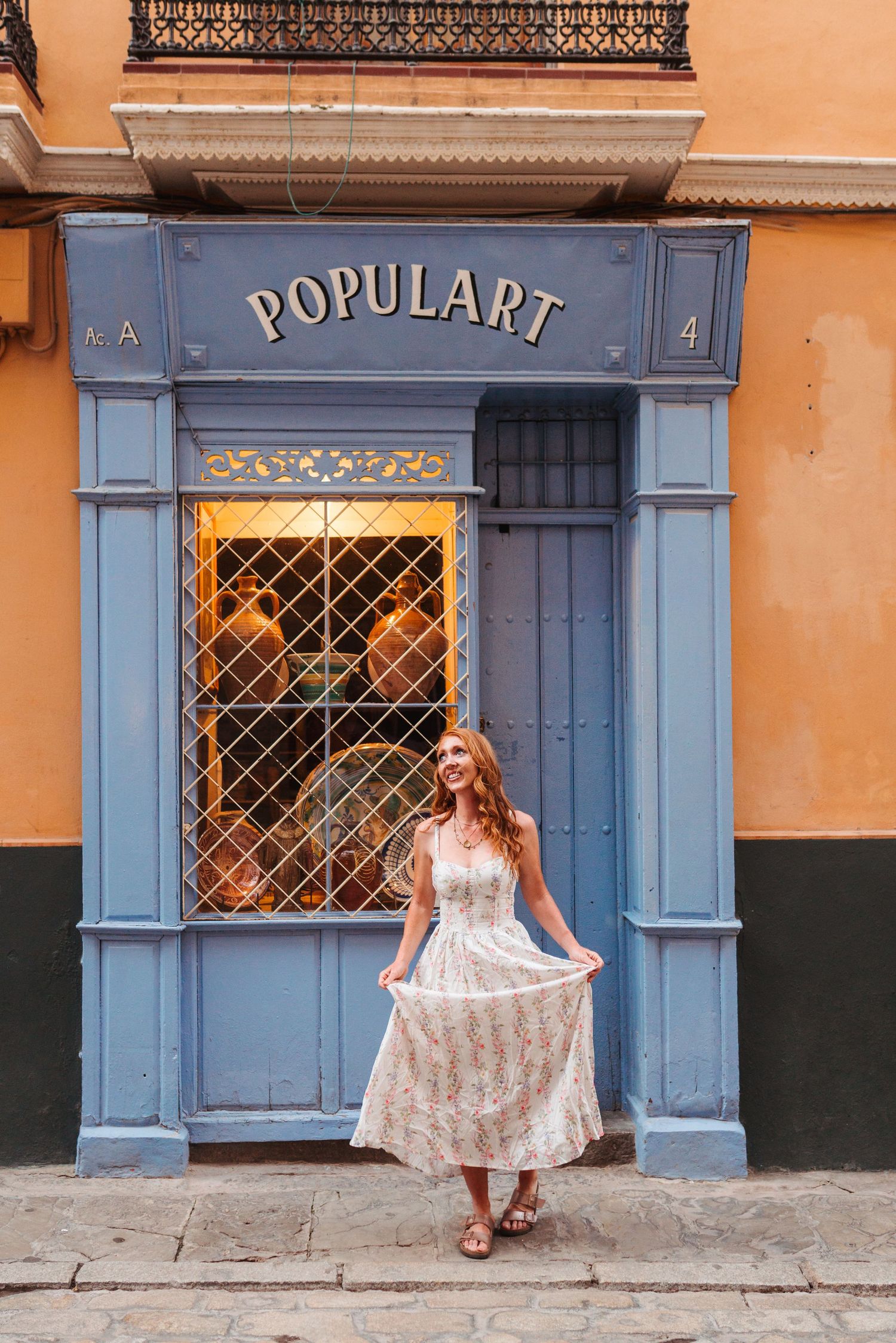 Redhead woman in floral dress posing in front of blue Populart storefront in Seville.