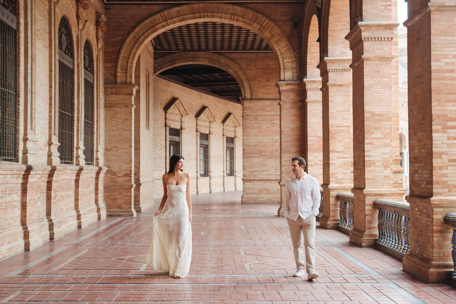 Newlywed couple strolling through elegant brick arched corridor at Plaza de Espana Seville.