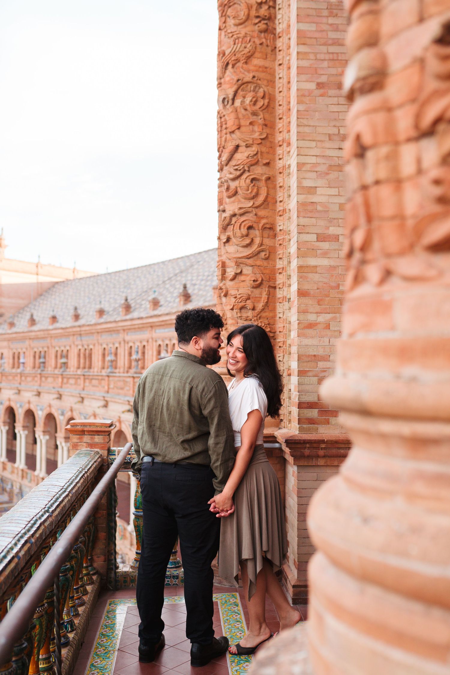Romantic couple sharing an intimate moment on ornate balcony of Plaza de España, Seville, Spain.