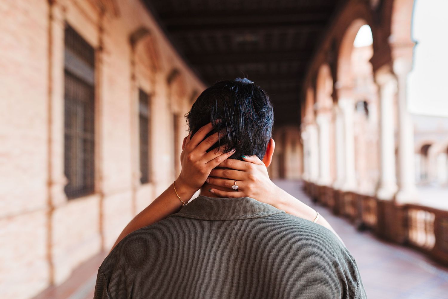 A person viewed from behind with a hand gently resting on their neck in an ornate archway corridor.