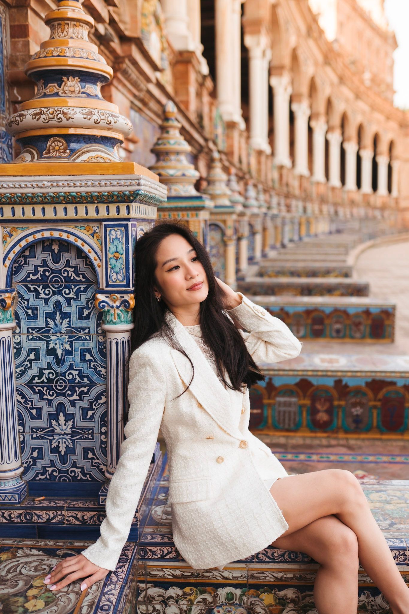 Woman in white tweed jacket sitting by colorful mosaic tiles at Plaza de España.