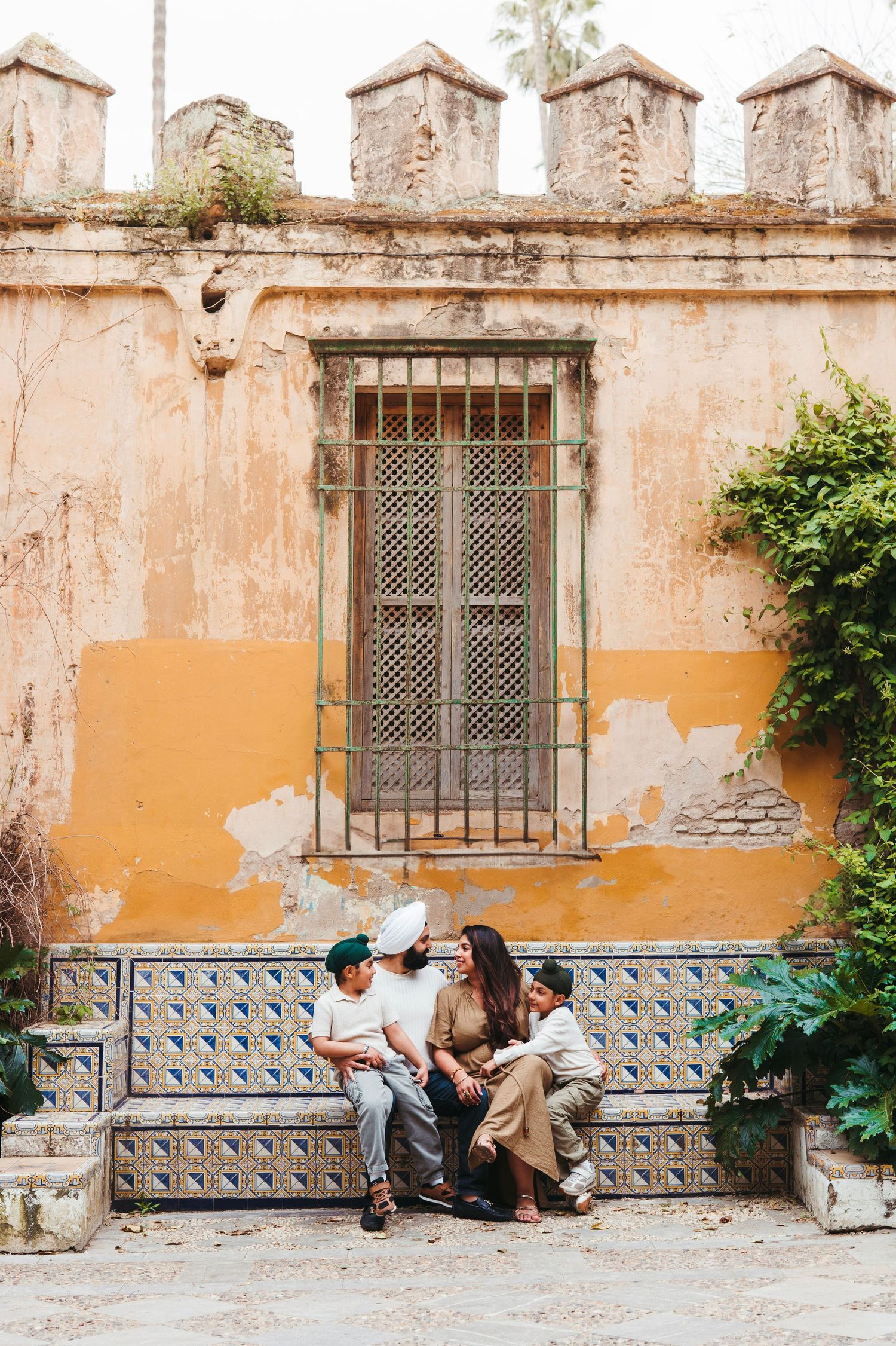 Family of four sitting on tiled bench before rustic yellow wall in Seville, Spain.