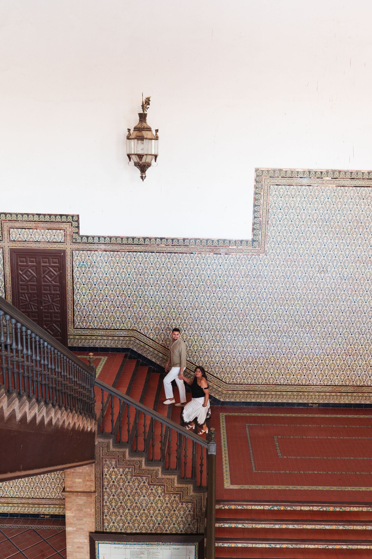 Couple descending ornate Moroccan-style staircase with intricate tilework walls and traditional brass lantern.