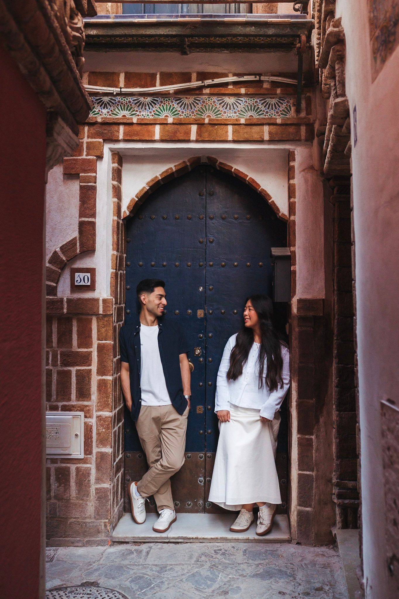 Couple standing together in front of a decorative Moorish arched wooden door.