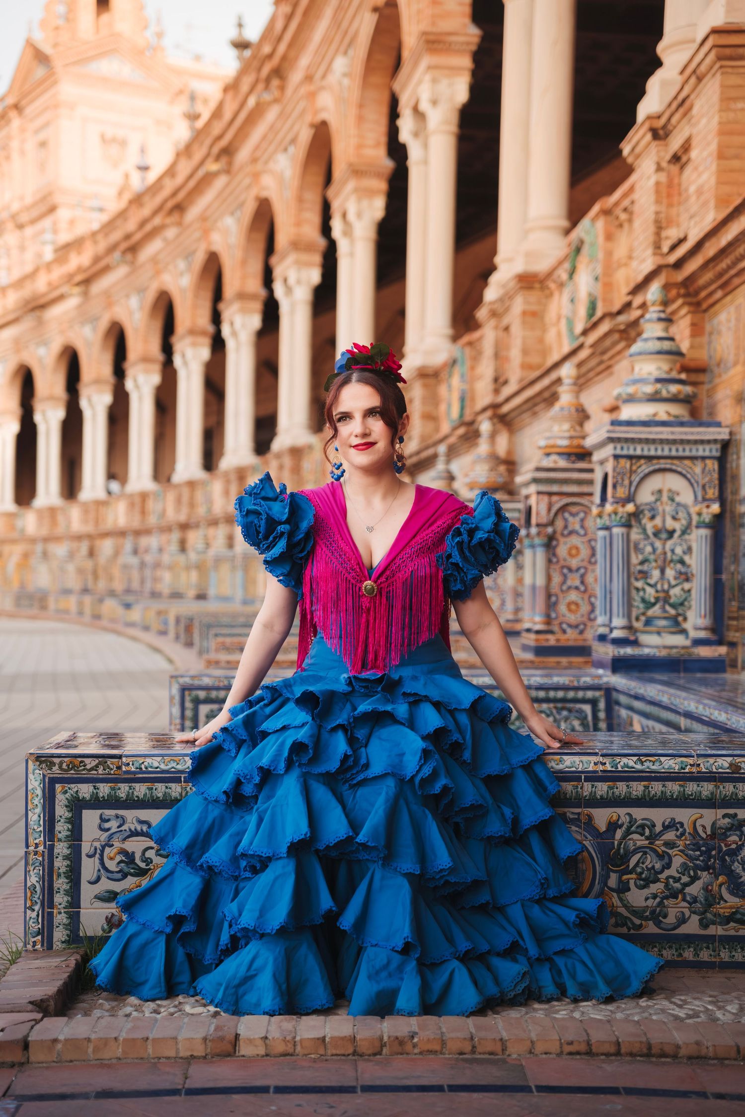 Woman in blue and pink flamenco dress sits at Plaza de Espana in Seville, Spain.
