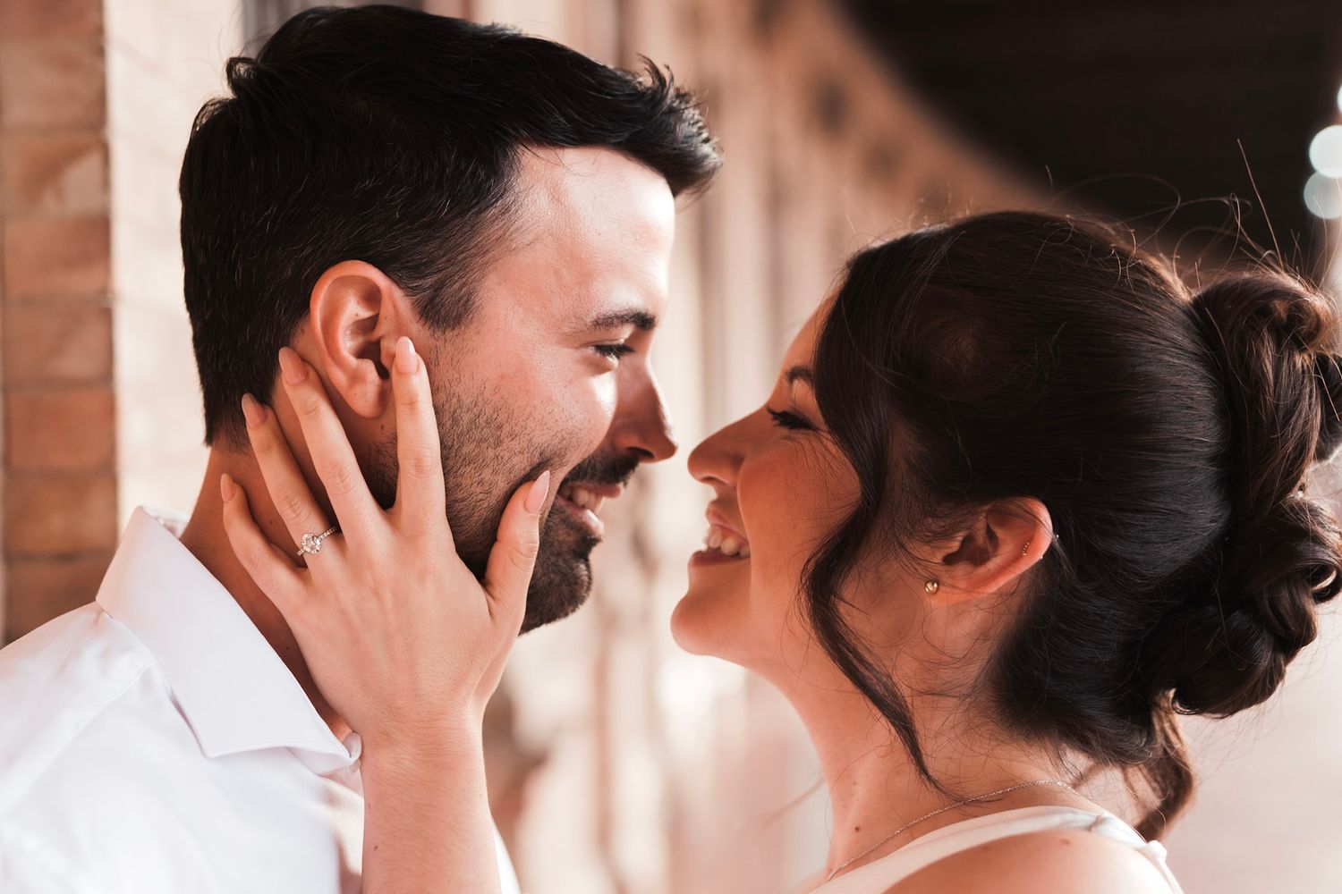 Joyful couple sharing an intimate moment, woman with updo touching mans face tenderly while smiling.