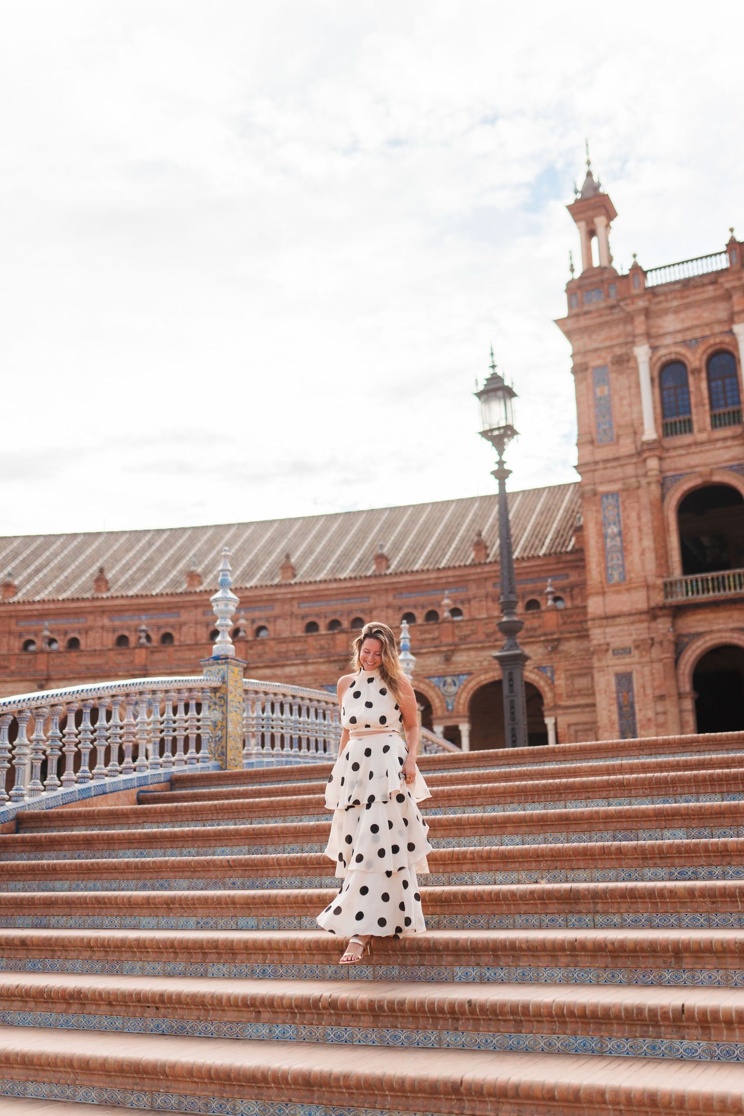 Woman in polka dot dress walking down ornate steps at Plaza de España, Seville, Spain.