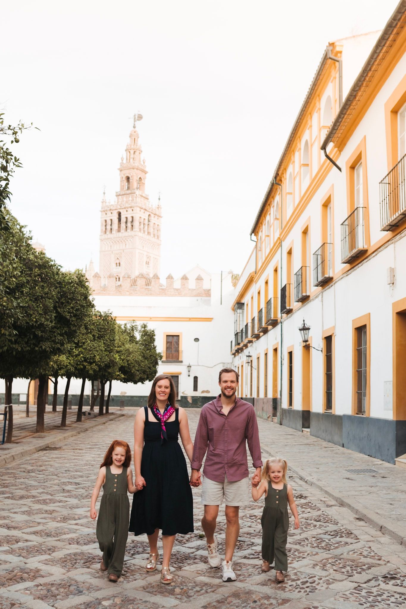 A happy family of four walking on cobblestone streets with the Giralda tower in the background.