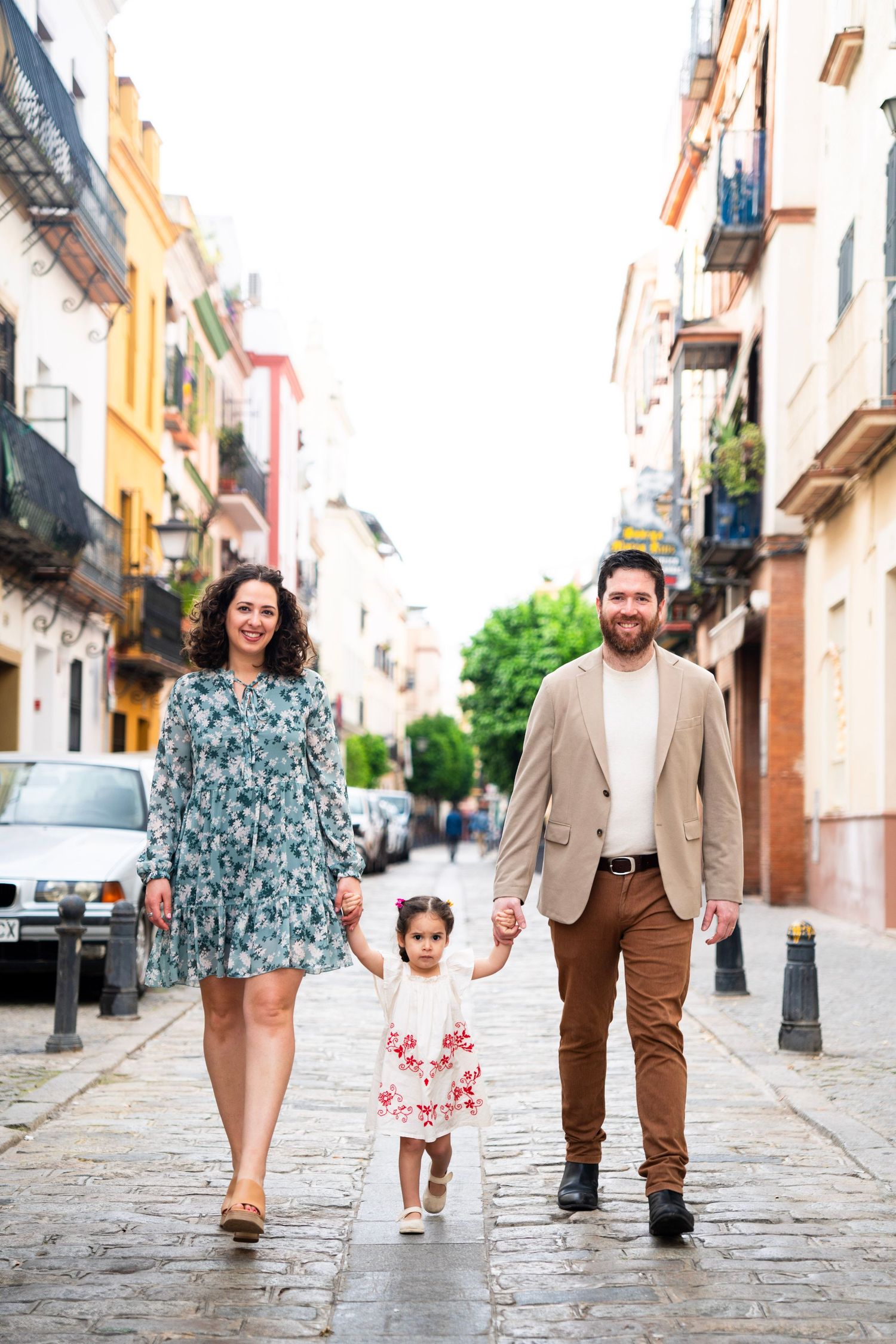 Smiling family with young daughter walks hand in hand along a charming cobblestone street in Seville.