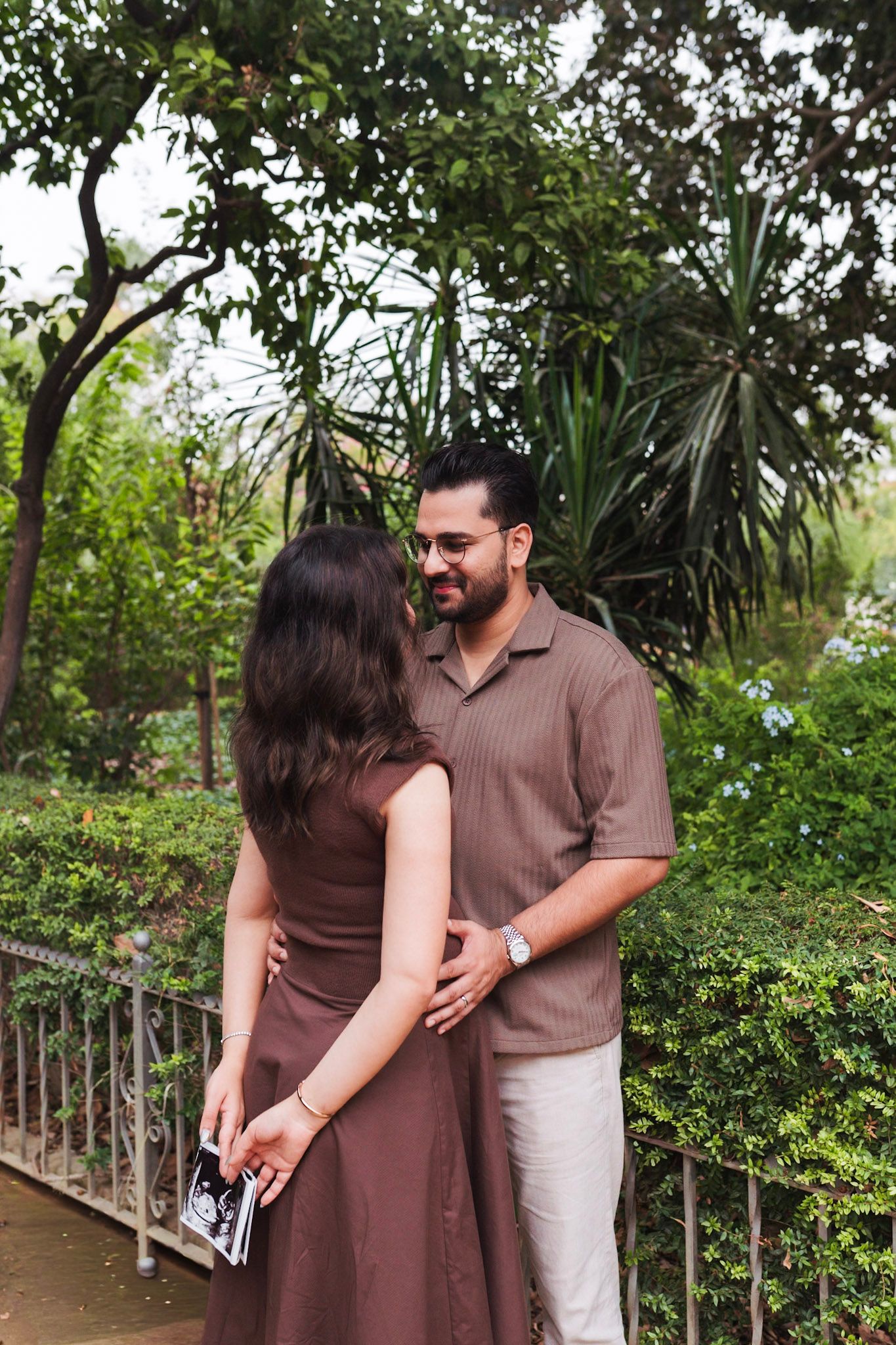 Expecting couple embracing in lush garden, woman holding ultrasound photo.