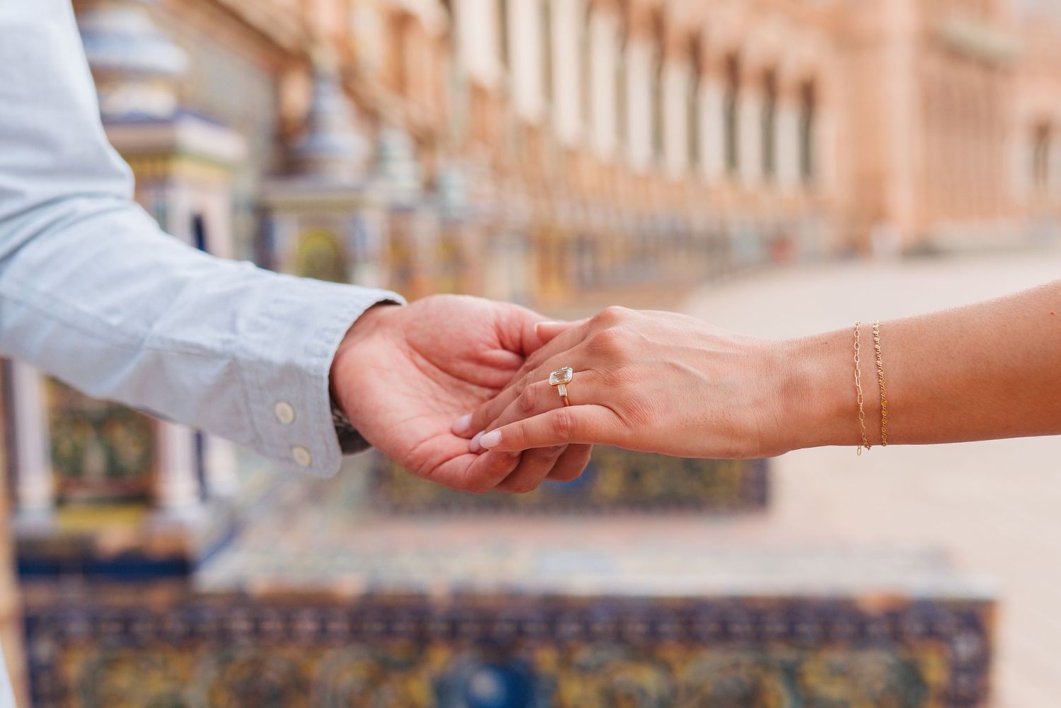 Couple holding hands with diamond engagement ring outdoors at Plaza de España in Seville, Spain.