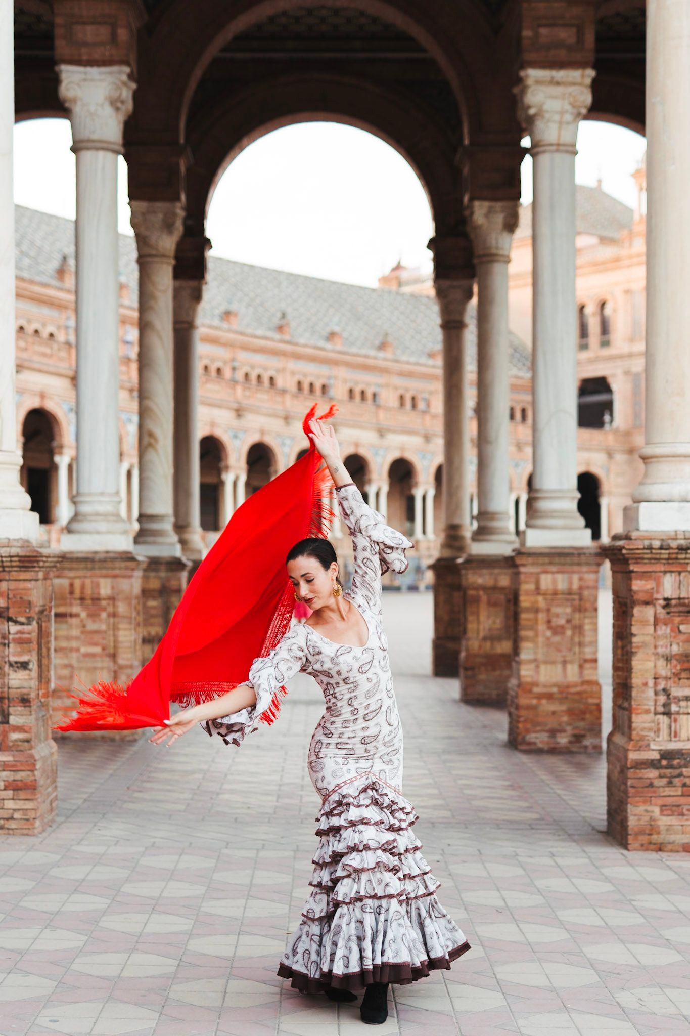 Flamenco dancer in white ruffled dress waving red shawl at Plaza de Espana, Seville.