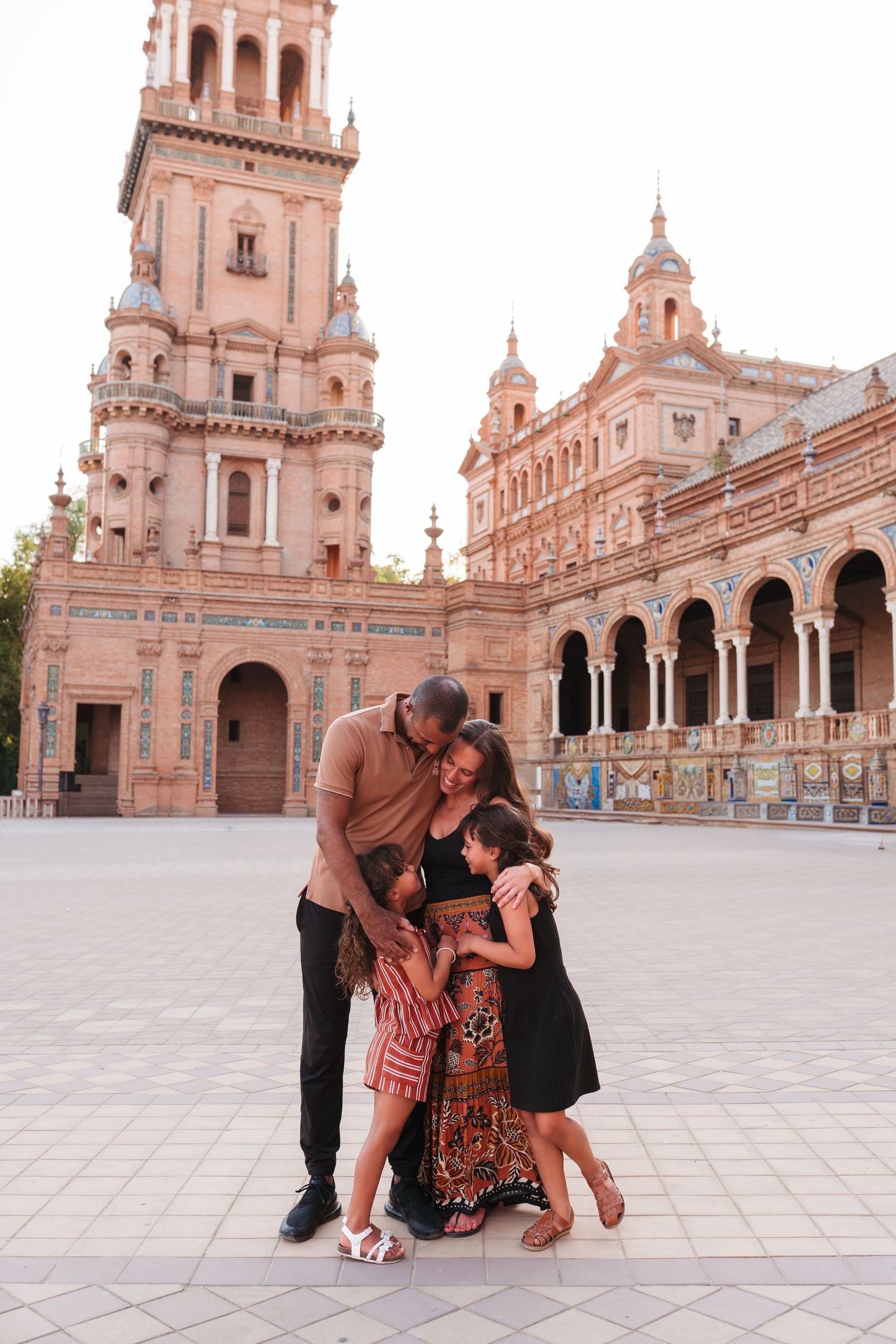 Family embracing at Plaza de España, Seville, with ornate Renaissance revival architecture and tower in background.