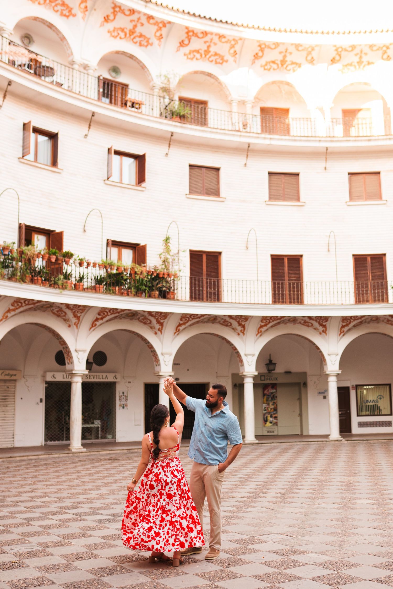 Couple dancing in a stunning circular courtyard with arched colonnades and ornate balconies in Seville, Spain.