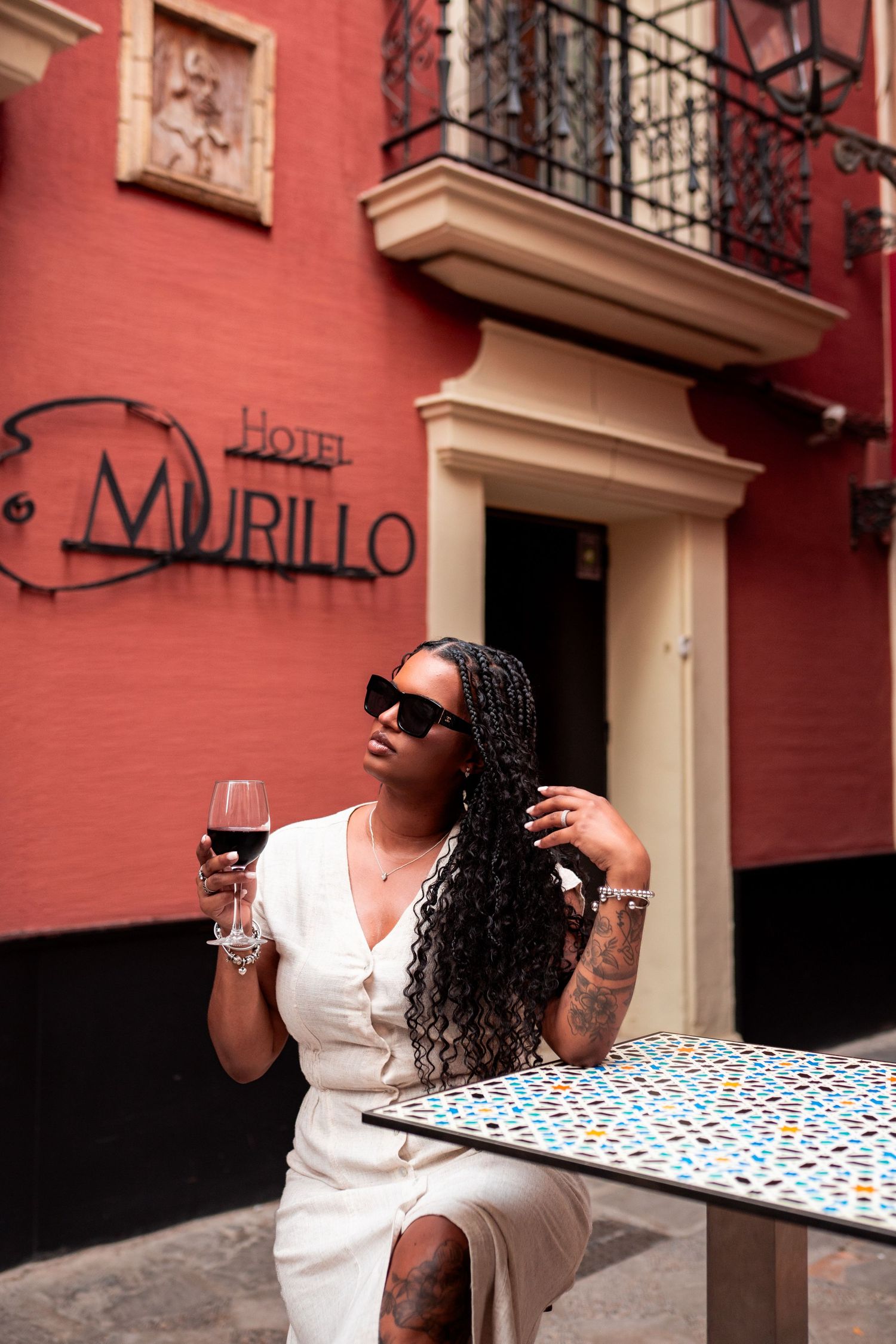 Woman in white dress sipping red wine at Hotel Murillo outdoor cafe in Seville, Spain.