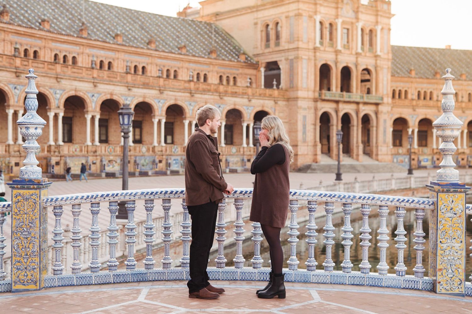 Engaged couple standing together on decorated bridge at Plaza de Espana in Seville, Spain.