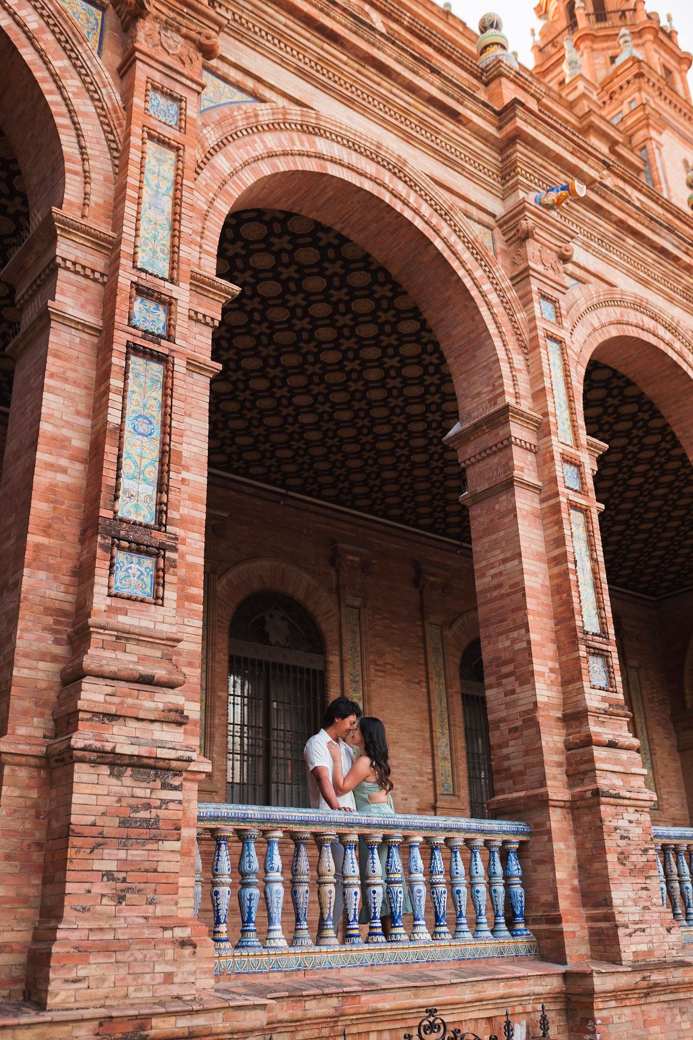 Couple kissing on ornate balcony of Plaza de Espana brick arcade in Seville, Spain.