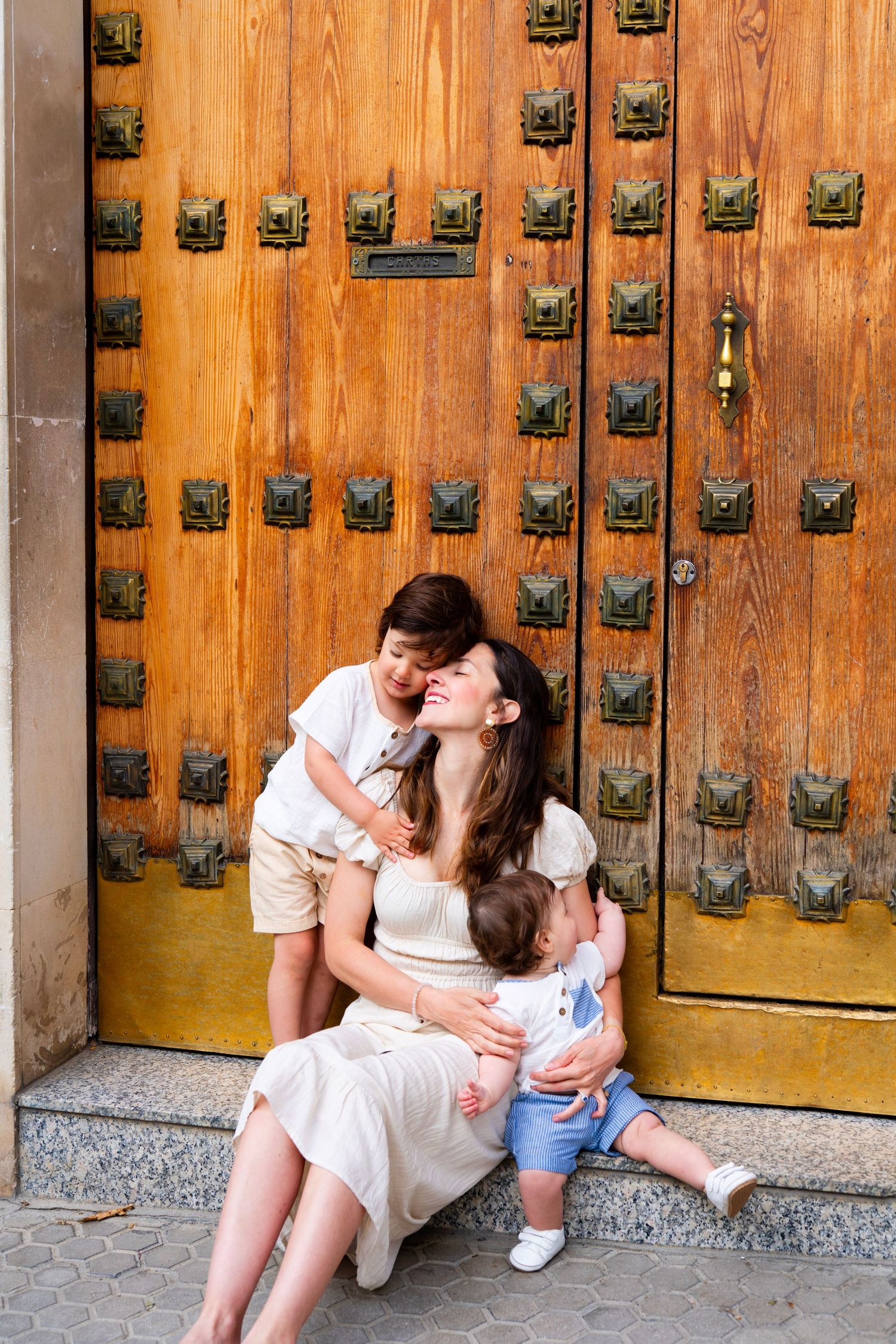 Mother sitting with two young children in front of ornate wooden door in Seville.
