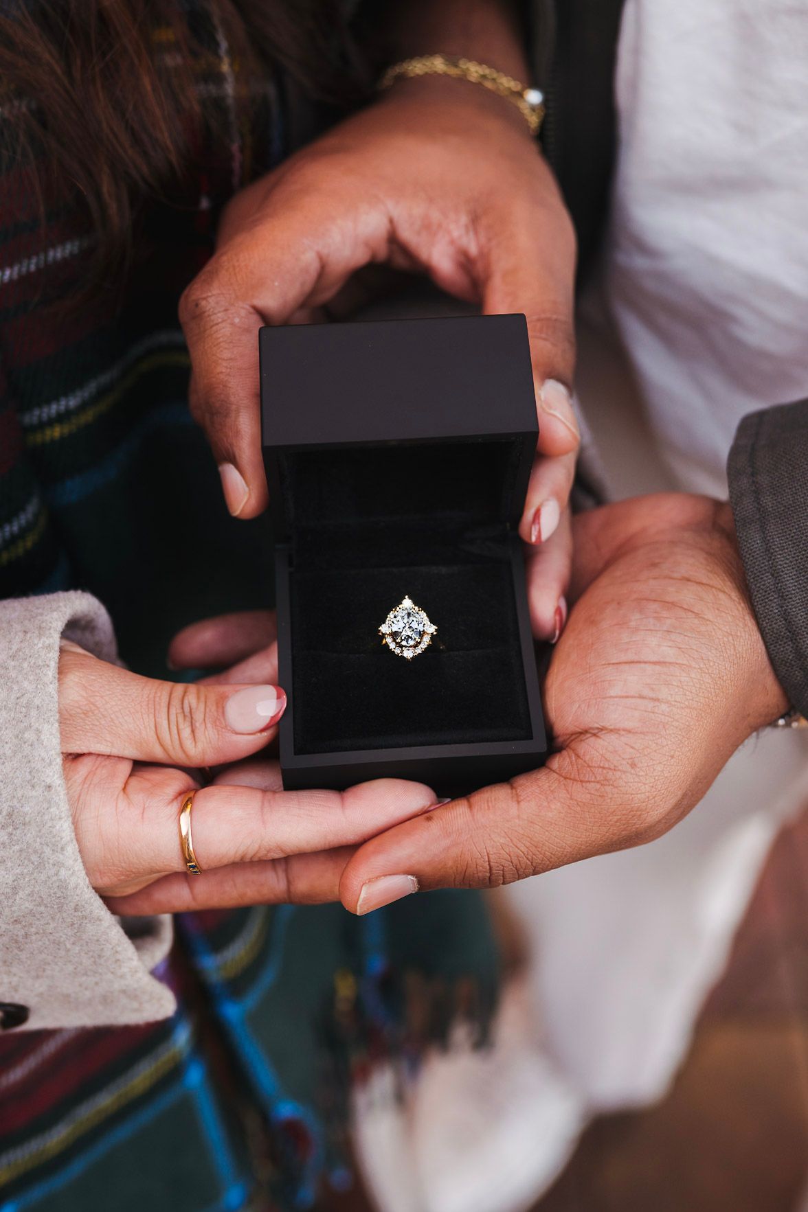 Hands holding open black jewelry box with diamond engagement ring during proposal moment.