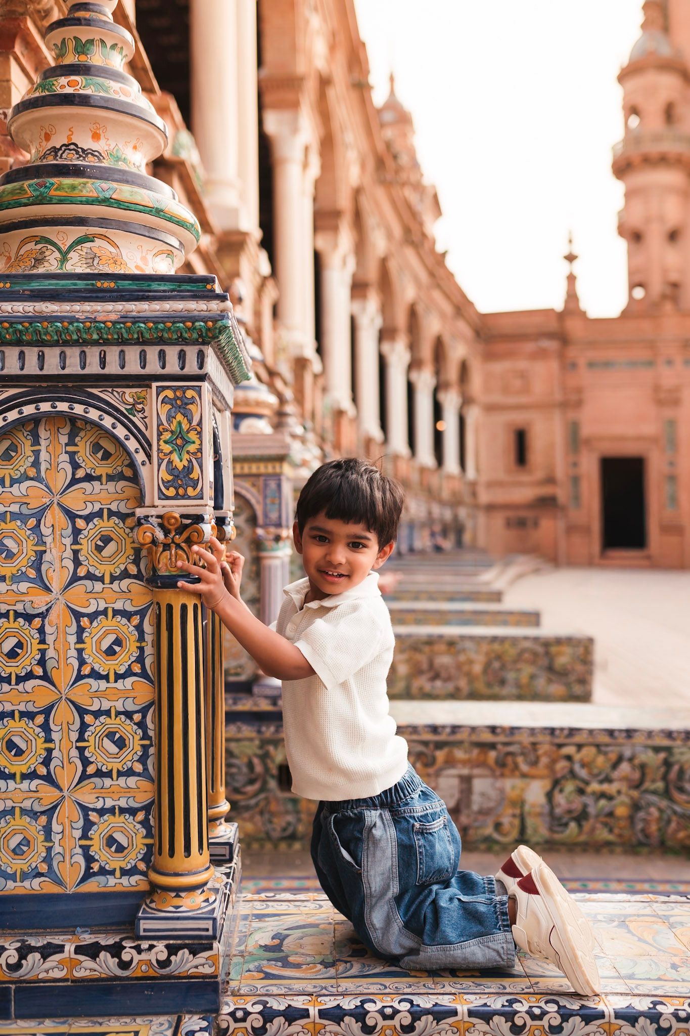 A young boy kneels on a colorful tiled bench at the ornate Plaza de Espana in Seville Spain.